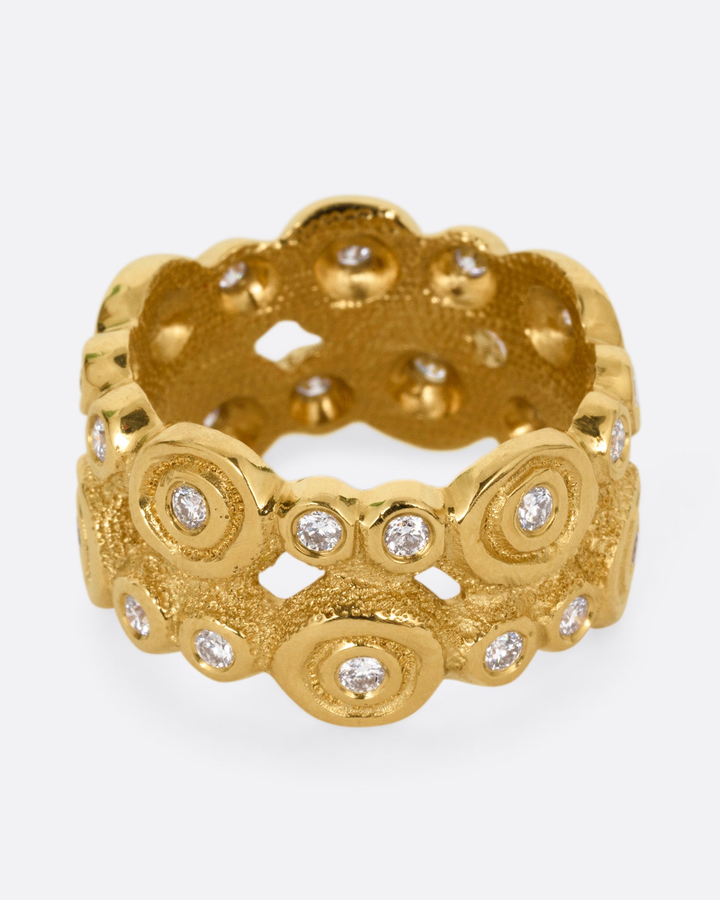 A wide yellow gold ring with brilliant cut diamonds nestled in bezel settings, shown from the front.