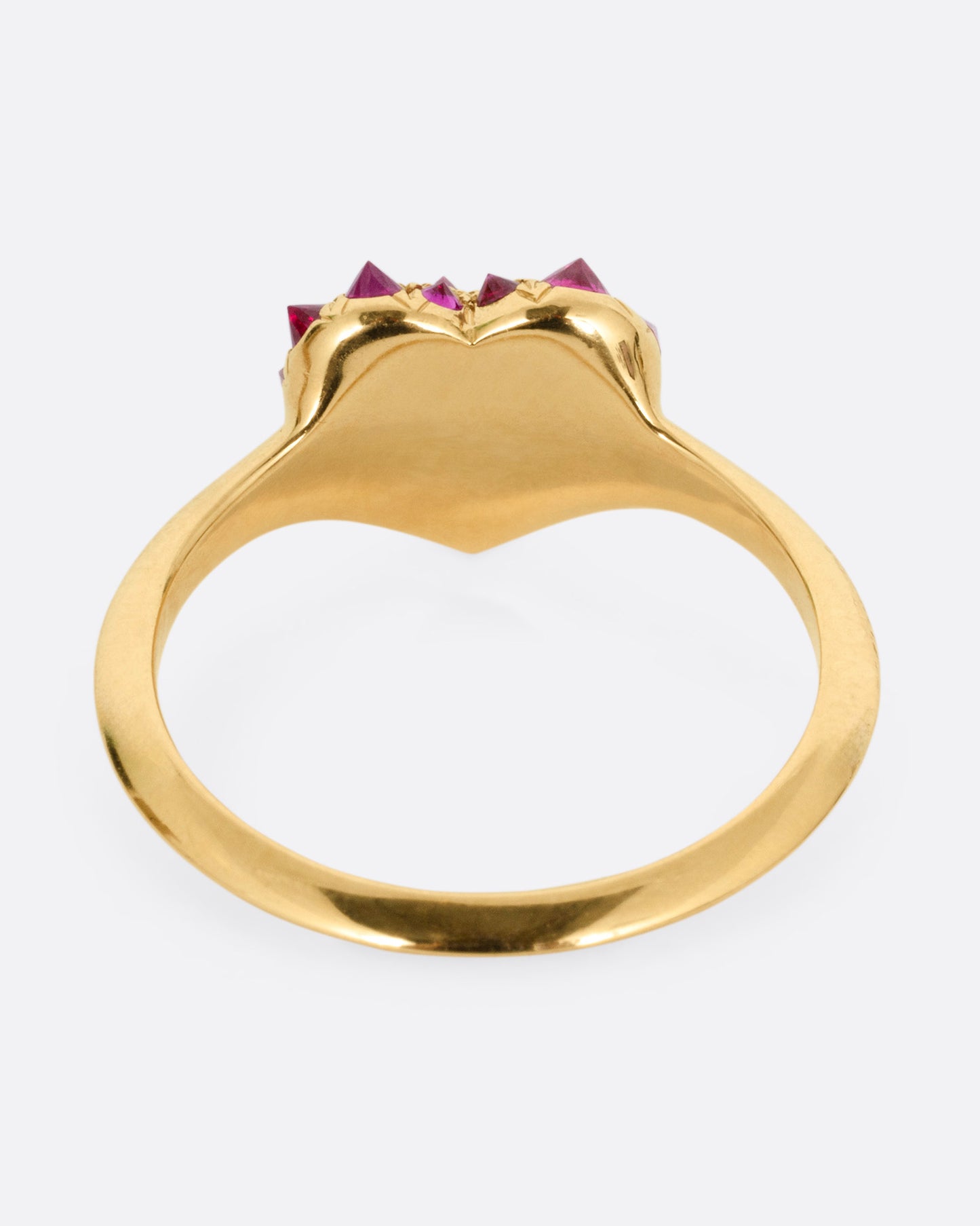 A yellow gold ring with a heart peppered with reverse set rubies of varying sizes, shown from the back.