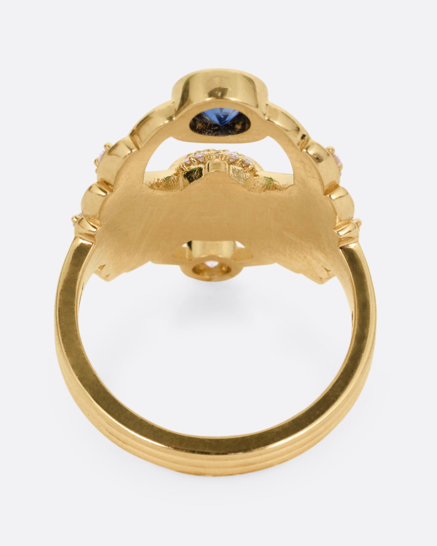 A yellow gold scarab ring with accents of white diamonds and a single blue sapphire between its fanned wings. Shown from the side.