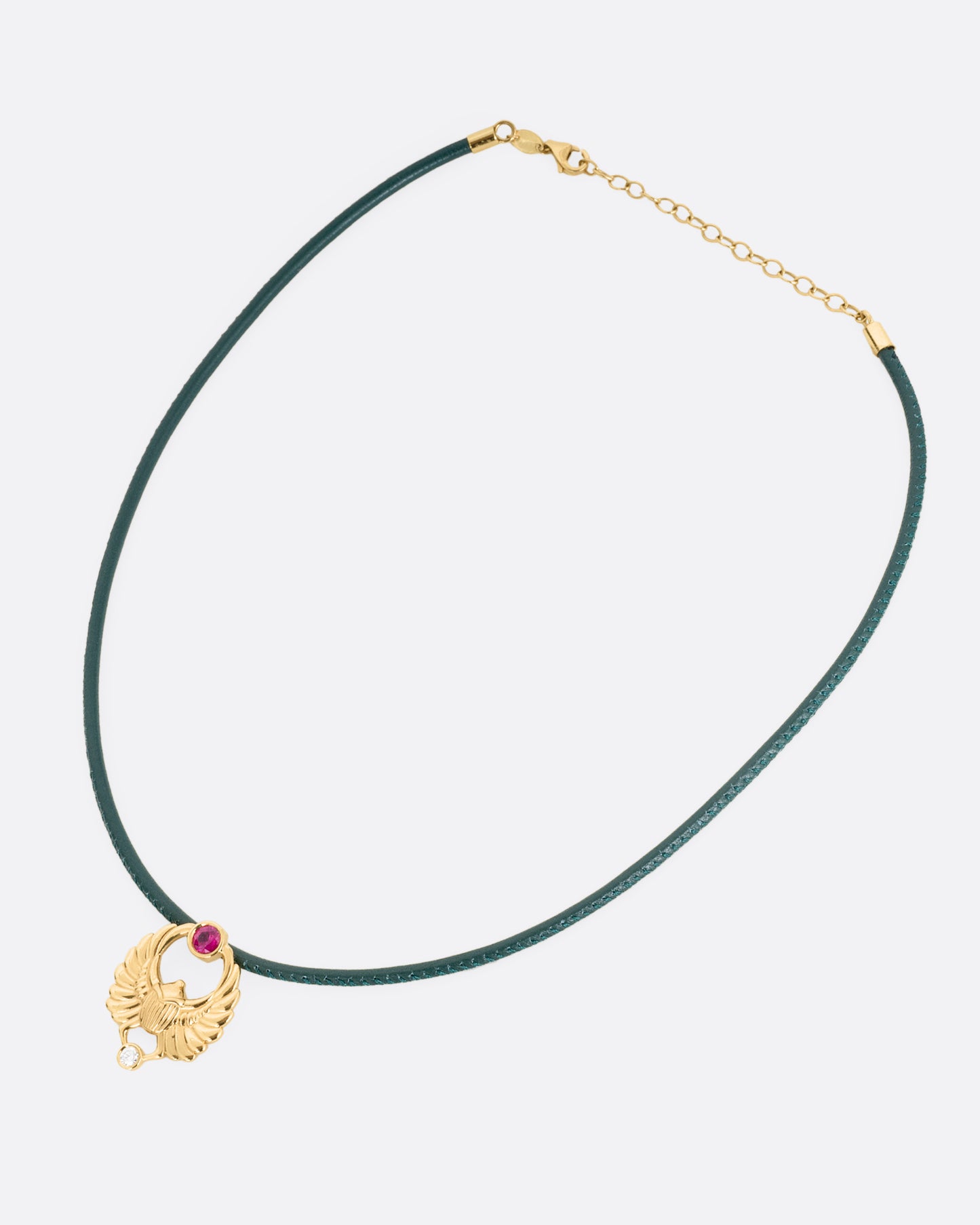 A yellow gold scarab pendant with a ruby and diamond, suspended from a green leather choker cord. Shown from the front.