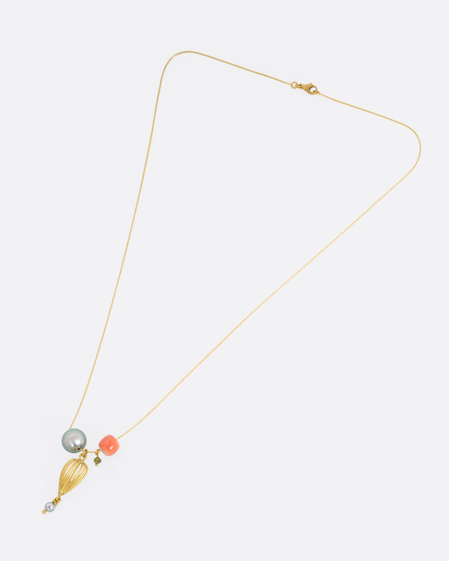 A yellow gold necklace with a gold pendant, Tahitian and Akoya pearls, a coral bead, and a green diamond bead, shown from the front.