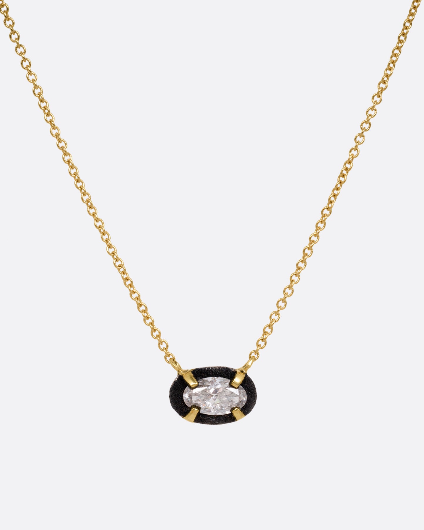 A yellow gold necklace with a pendant of darkened white gold surrounding a prong set diamond, shown from the front.