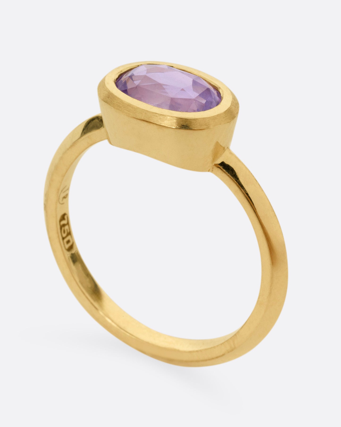 A yellow gold ring with a lilac sapphire, shown standing up from the side.