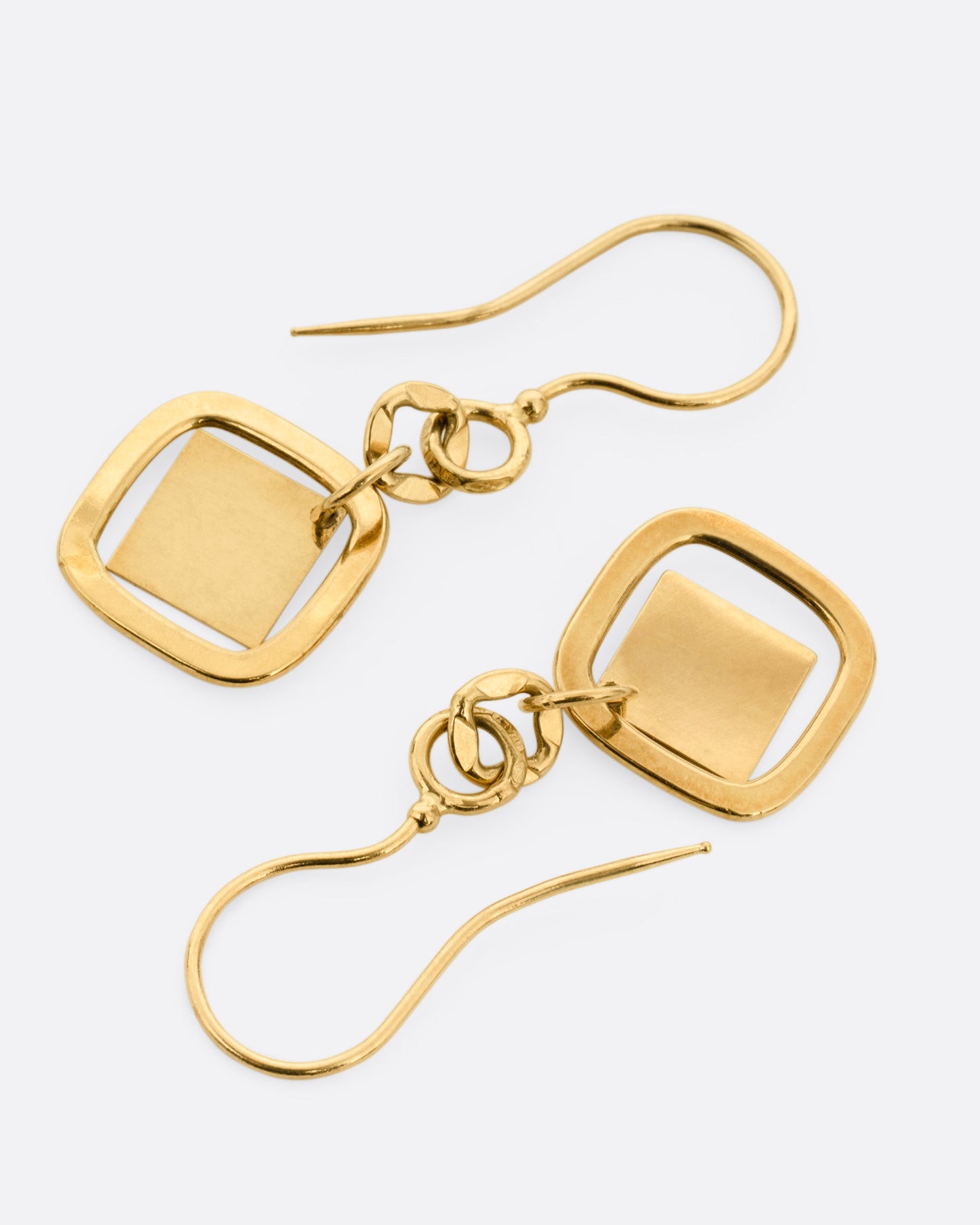 A pair of yellow gold drop earrings with diamond shaped dangles, shown lying flat.