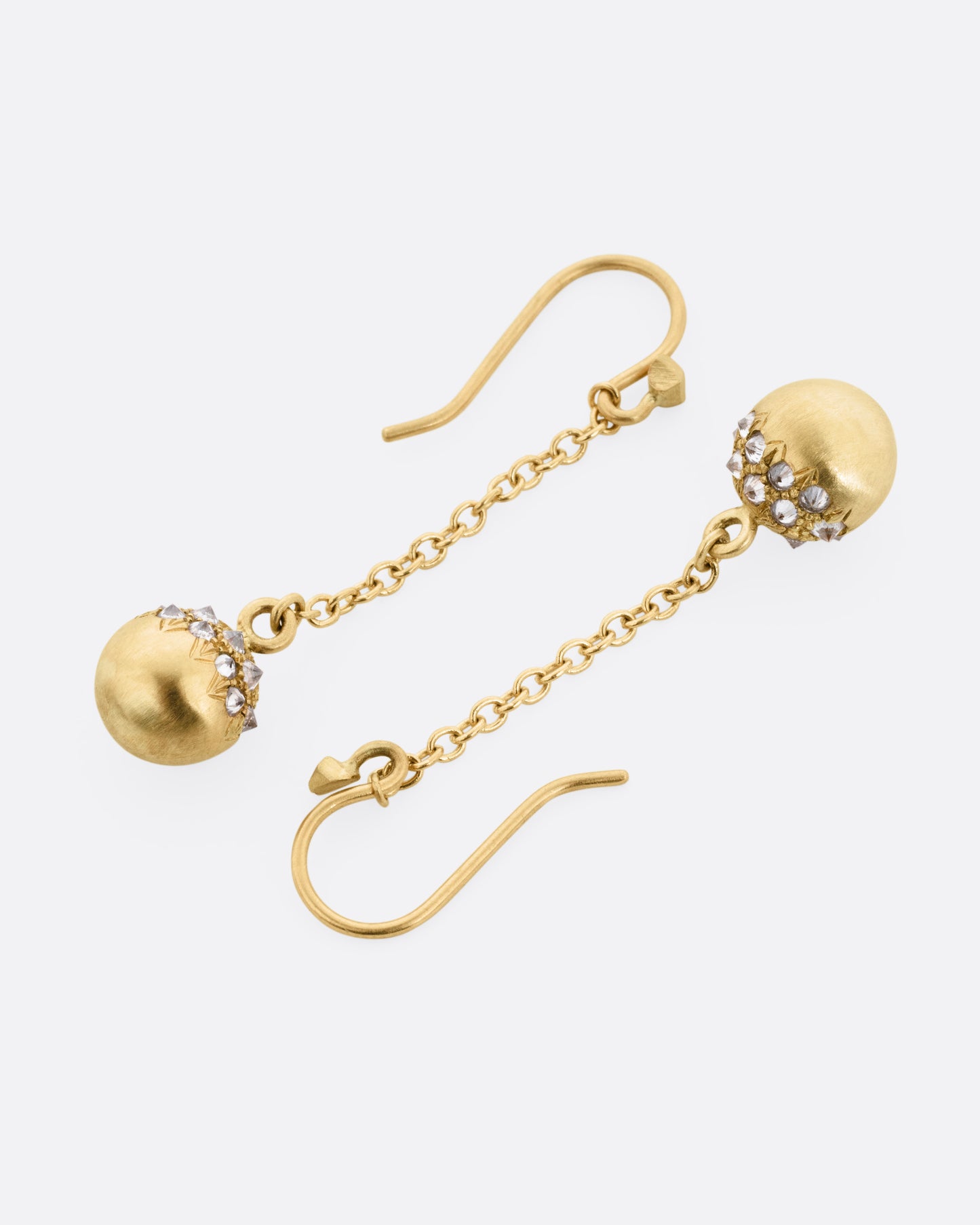 A pair of yellow gold drop earrings with lengths of gold cable chain ending in brushed gold spheres with reverse set grey diamonds. Shown lying on their sides.