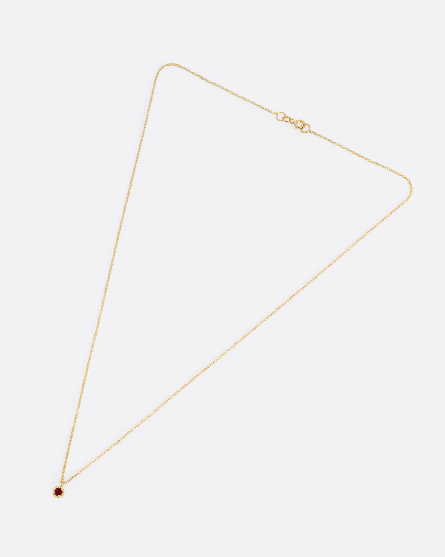 A yellow gold cable chain necklace with a prong set ruby, shown from the front.