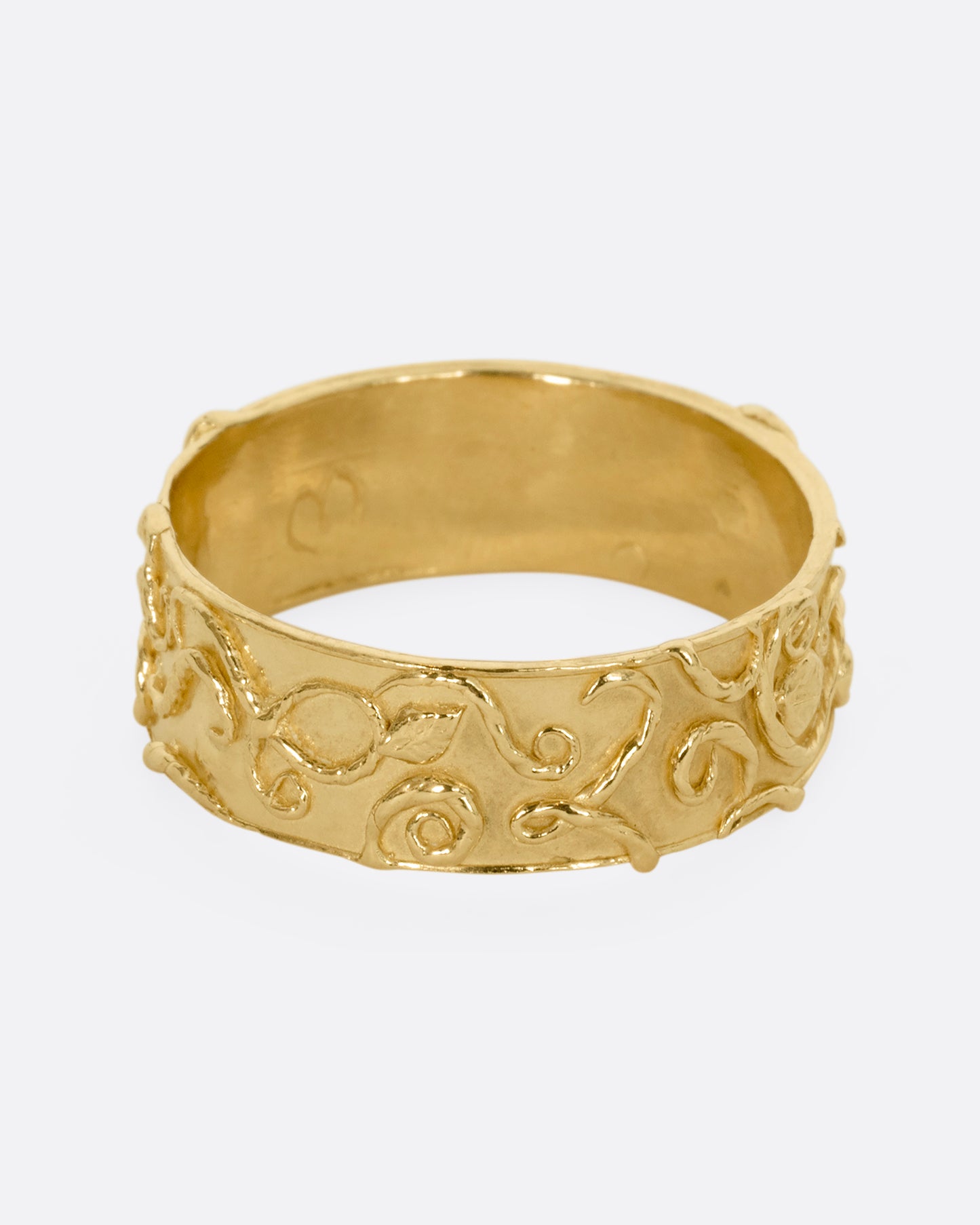 A yellow gold band ring wreathed in vines and leaves. Shown from the front.