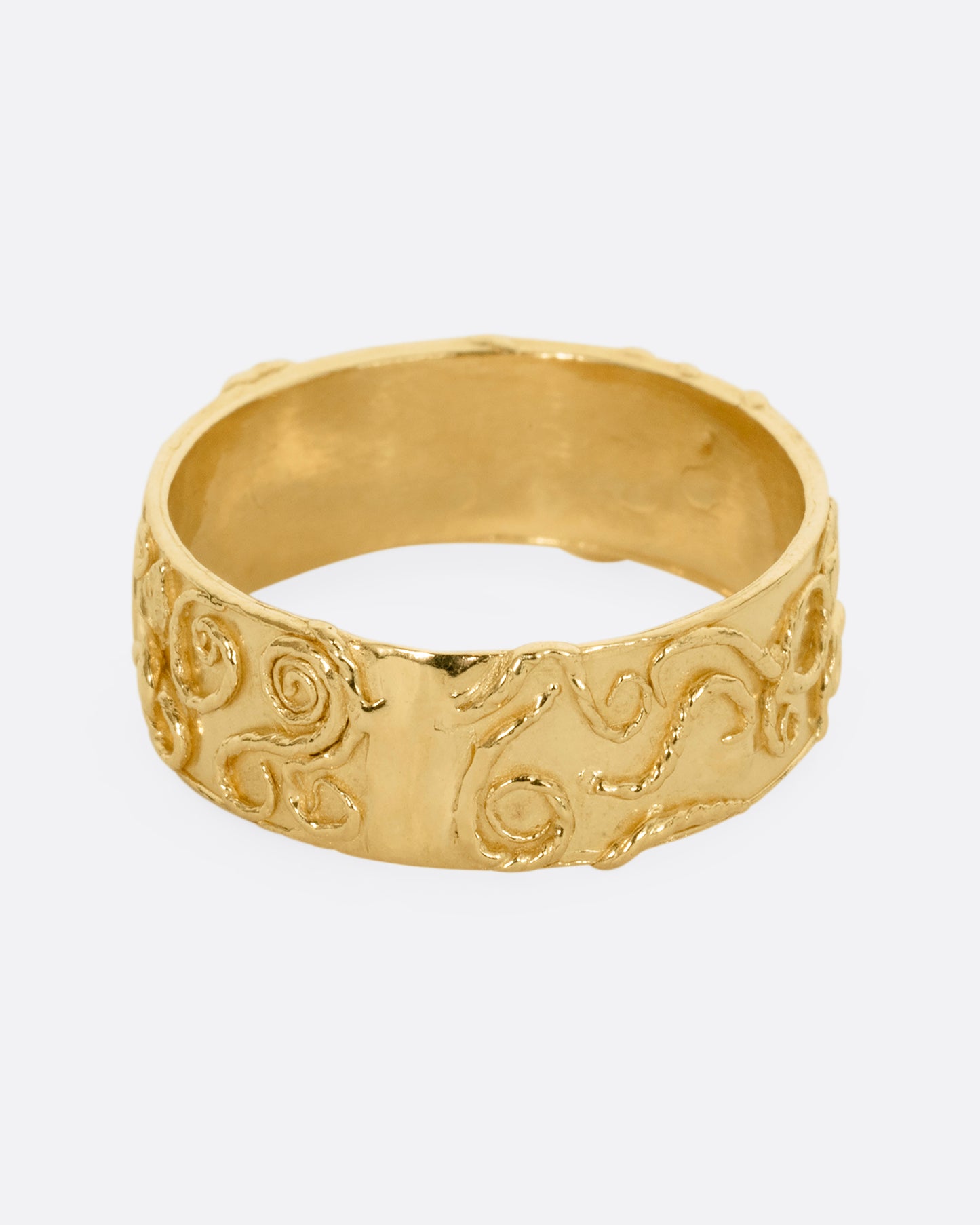 A yellow gold band ring wreathed in vines and leaves. Shown from the front.