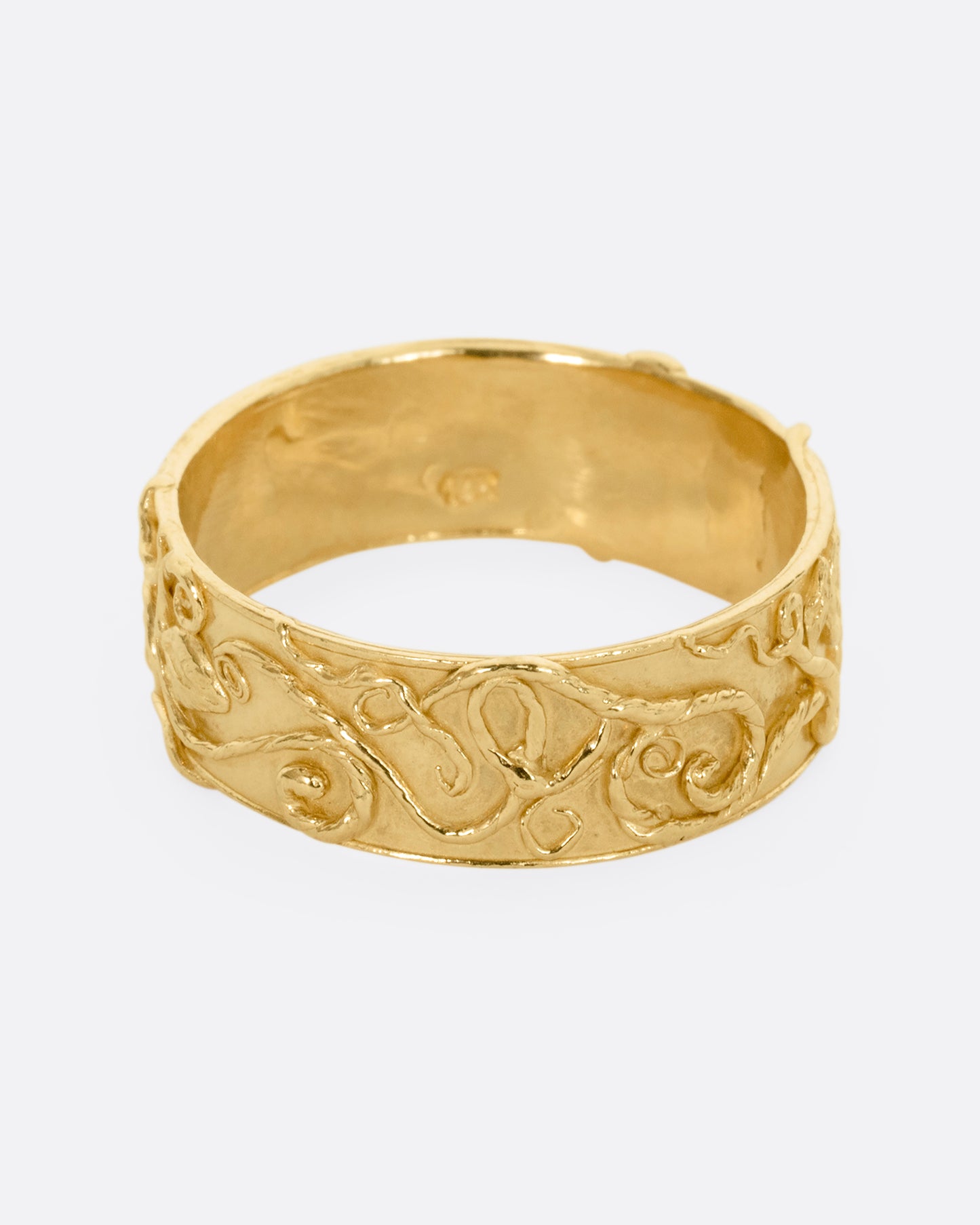 A yellow gold band ring wreathed in vines and leaves. Shown from the front.