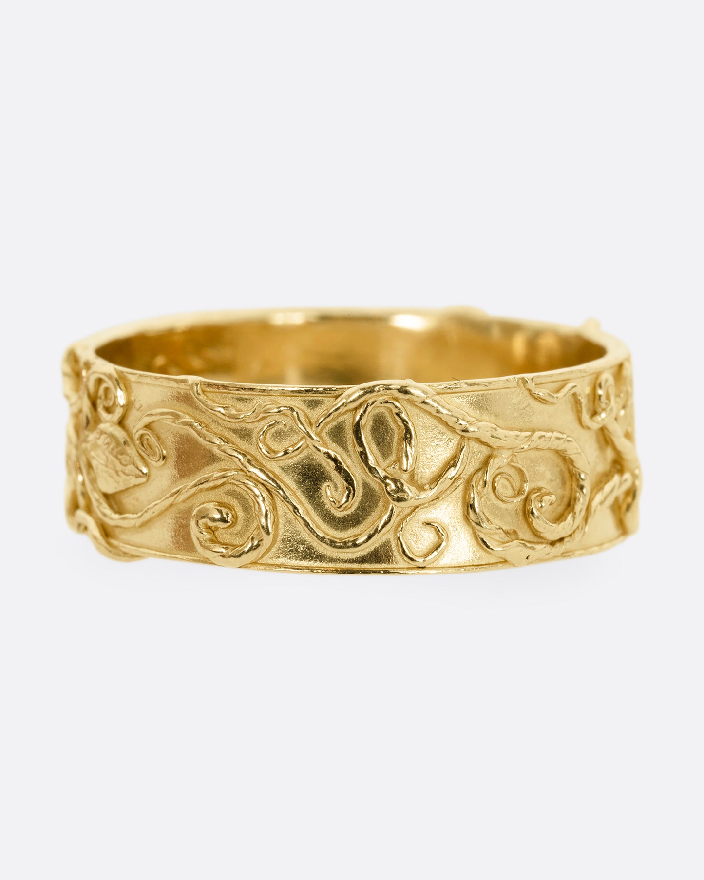 A yellow gold band ring wreathed in vines and leaves. Shown from the front.