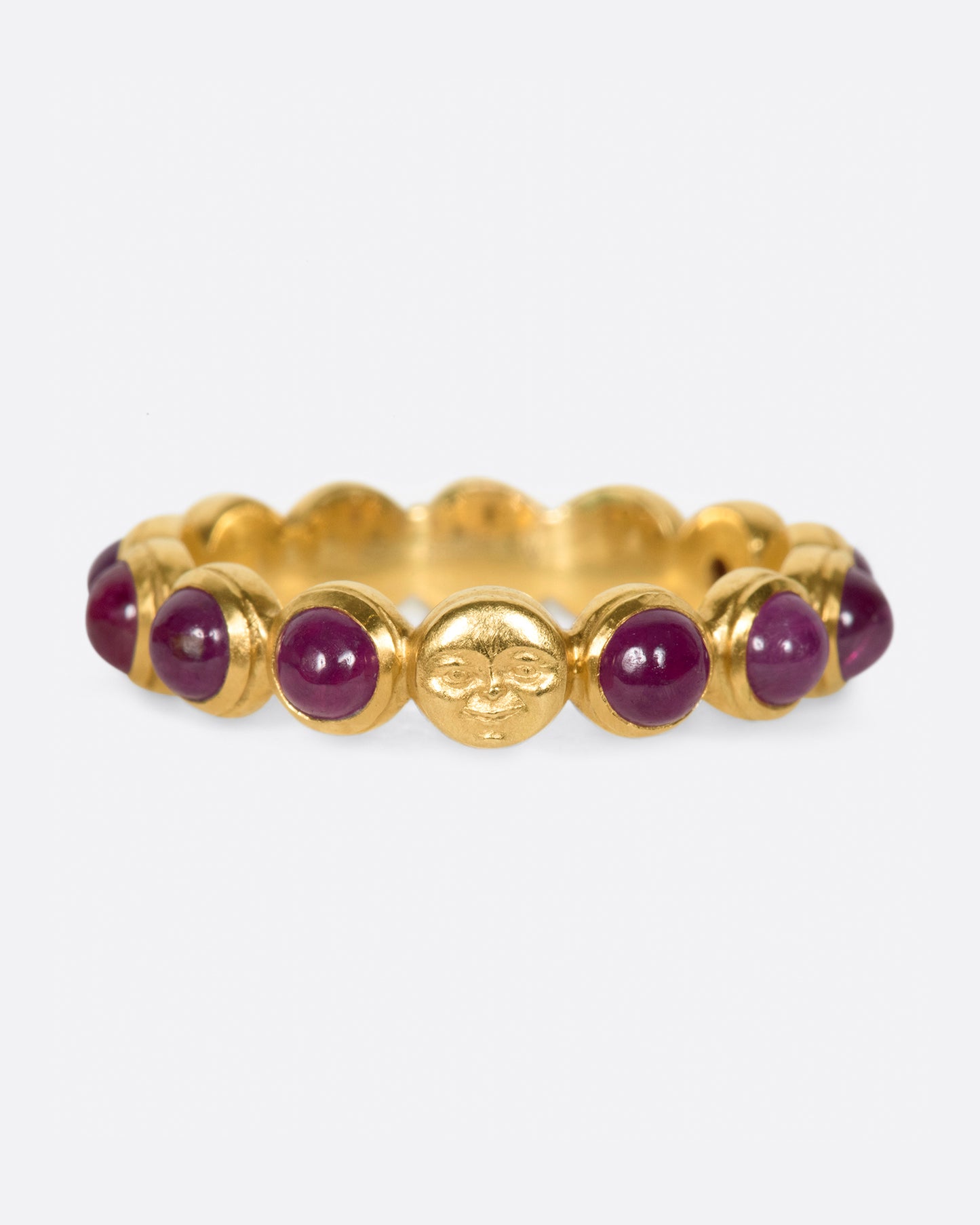 A yellow gold eternity band with ruby cabochons and one moonface. Shown from the front.