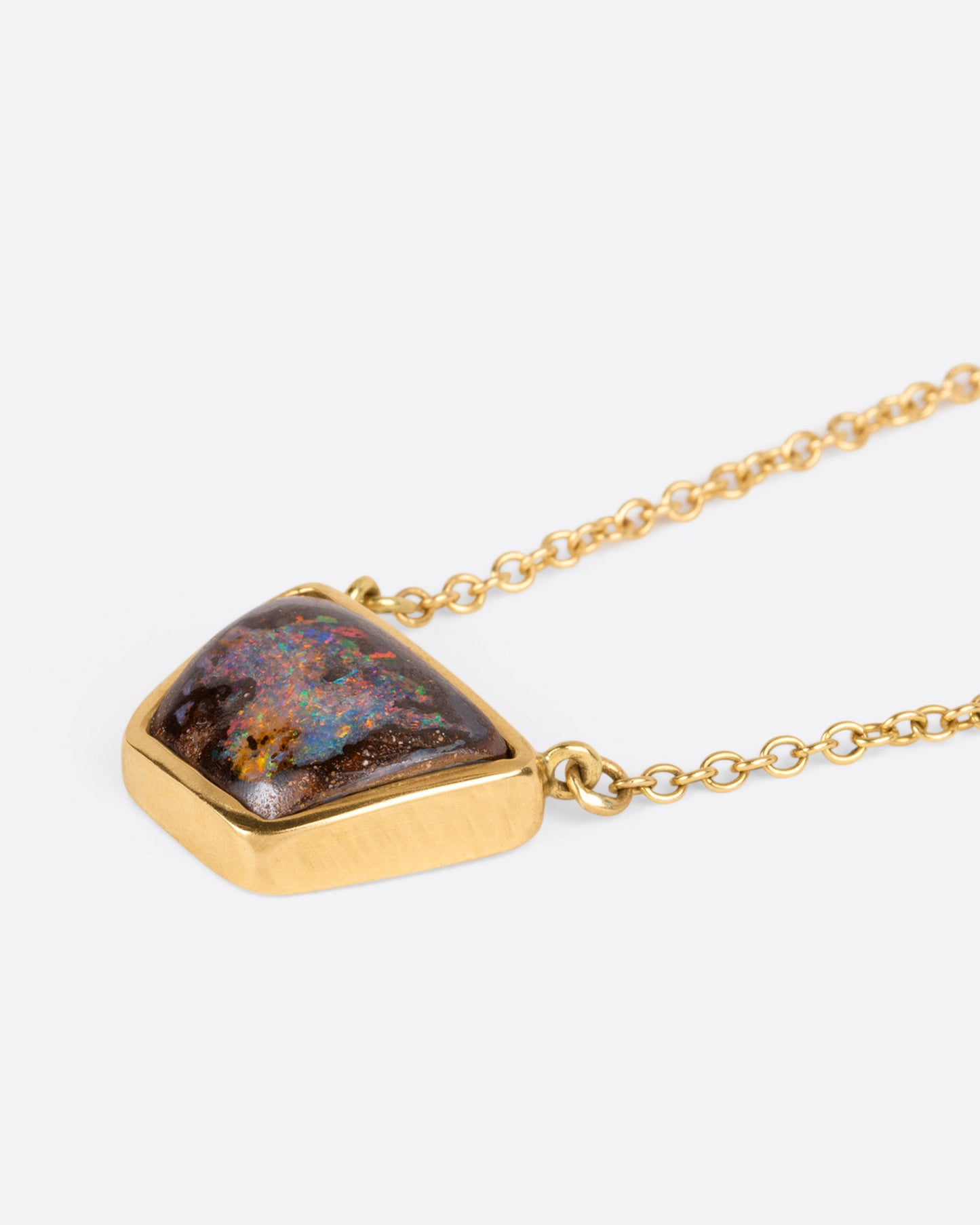 A yellow gold cable chain necklace with a trapezoidal opal set in a bezel. Shown from the side lying flat.