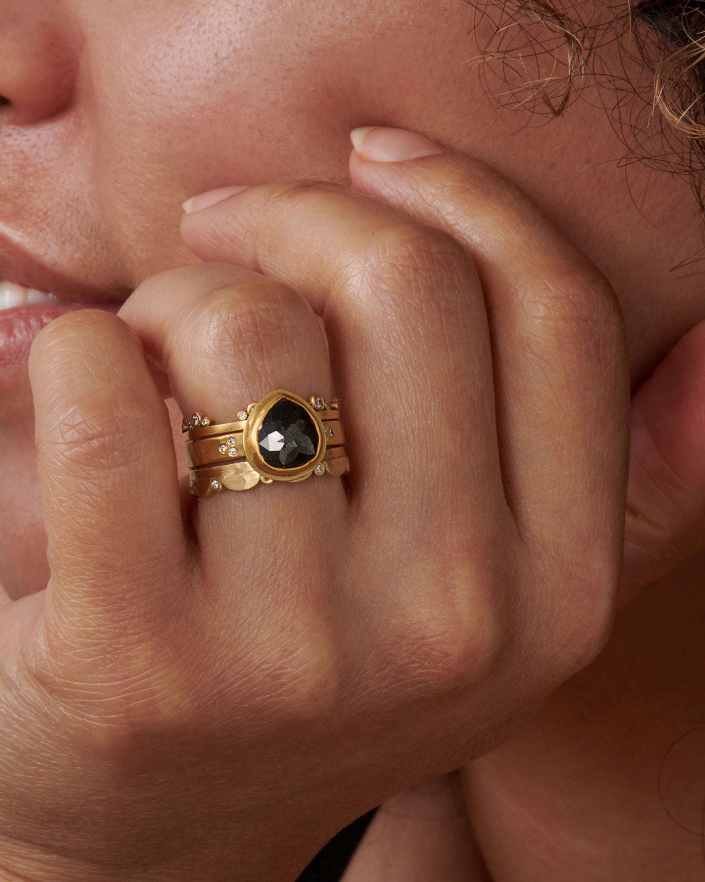 A delightful ring that's scalloped on one side, punctuated by sparkling inset diamonds, shown stacked with other rings.