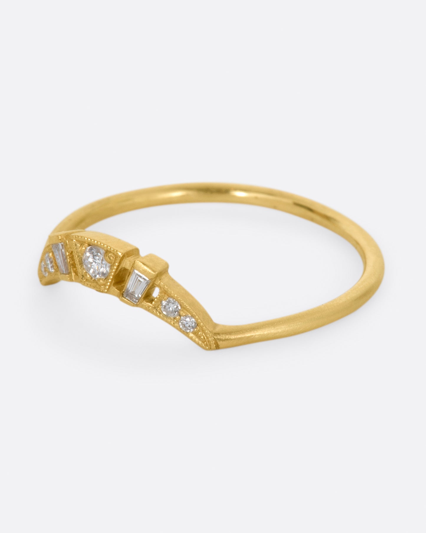 A yellow gold ring with a curved face that makes it good for stacking, dotted with round and baguette diamonds, and milgrain details - shown from the side.