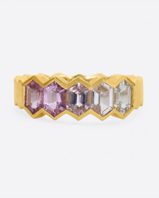 A yellow gold band ring with zigzag edges and five ombre pink sapphires channel set across the top.