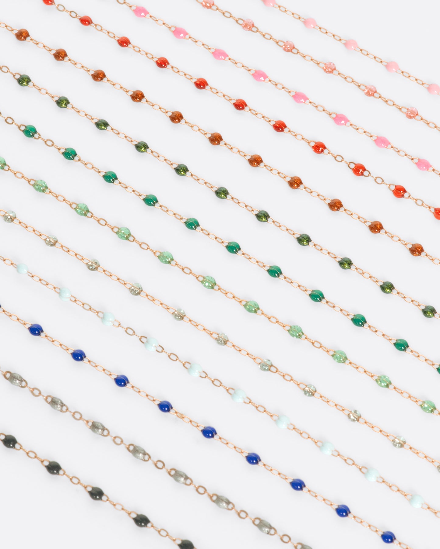 A close up view of yellow gold cable chain necklaces with multicolored resin droplets. Shown diagonally.