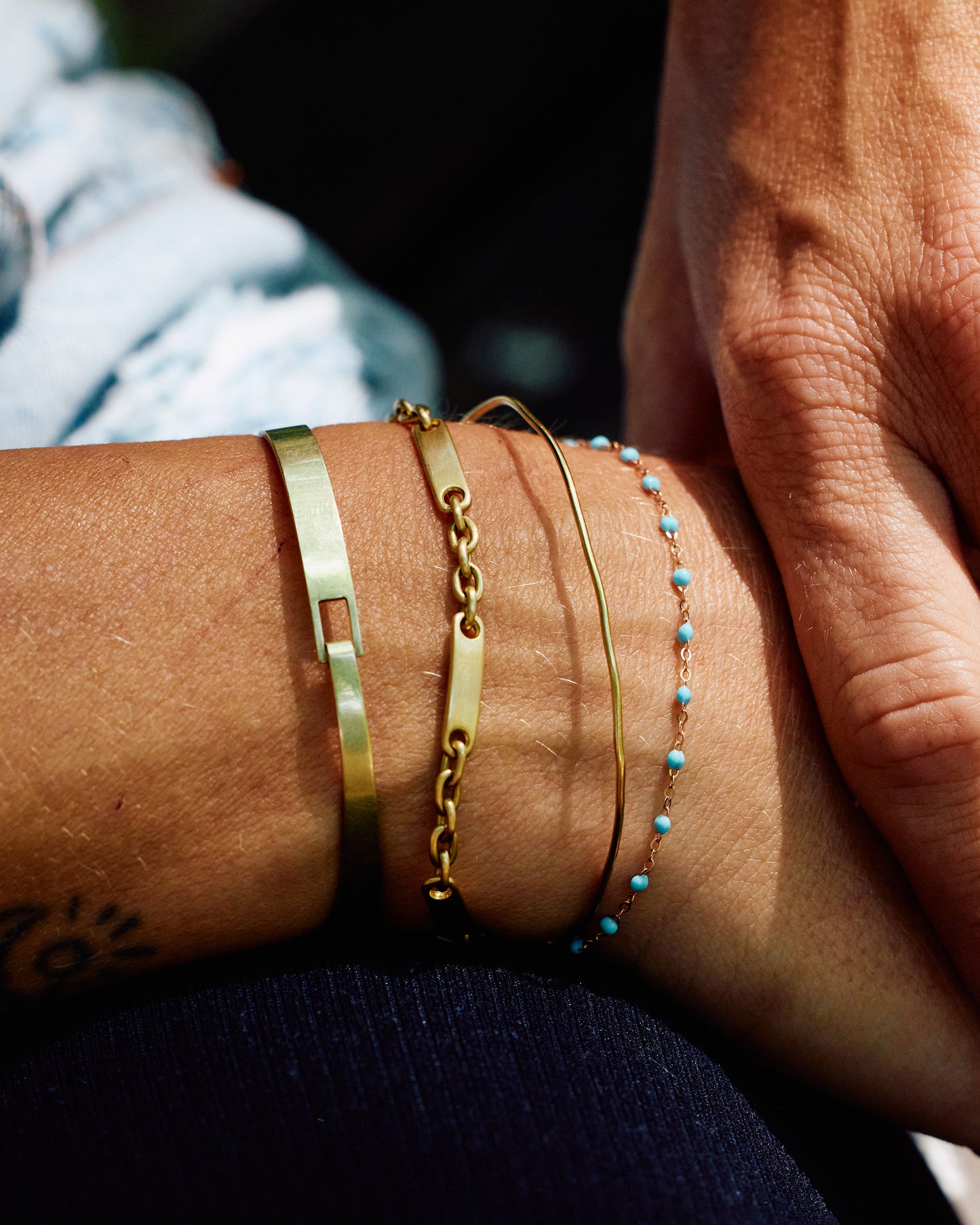 A wrist with four stacked bracelets. The first three (left to right) are gold and the fourth is a yellow gold cable chain bracelet with turquoise droplets.