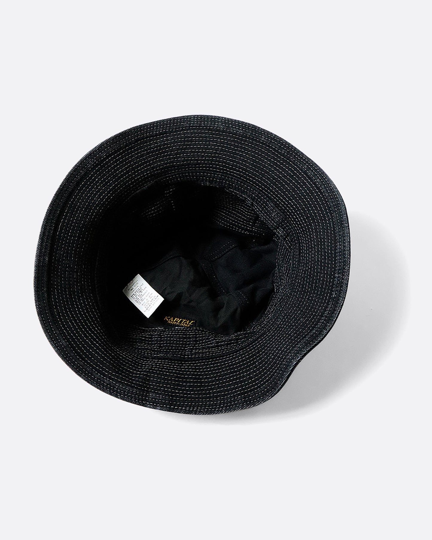 A black denim bucket hat with a buckle at the crown and contrast stitching throughout. View of the inside.