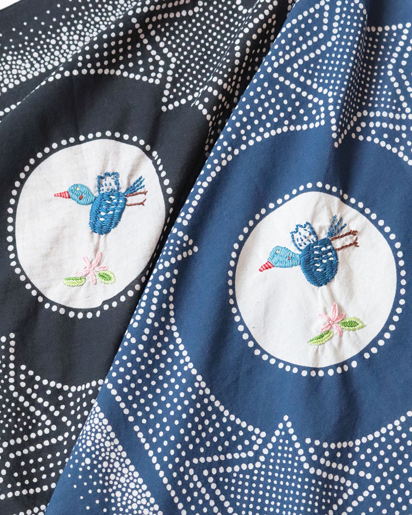 Two bandanas- one black and one navy with a white spotted star motif and a hand- embroidered magpie at the center. Shown close up from the front.