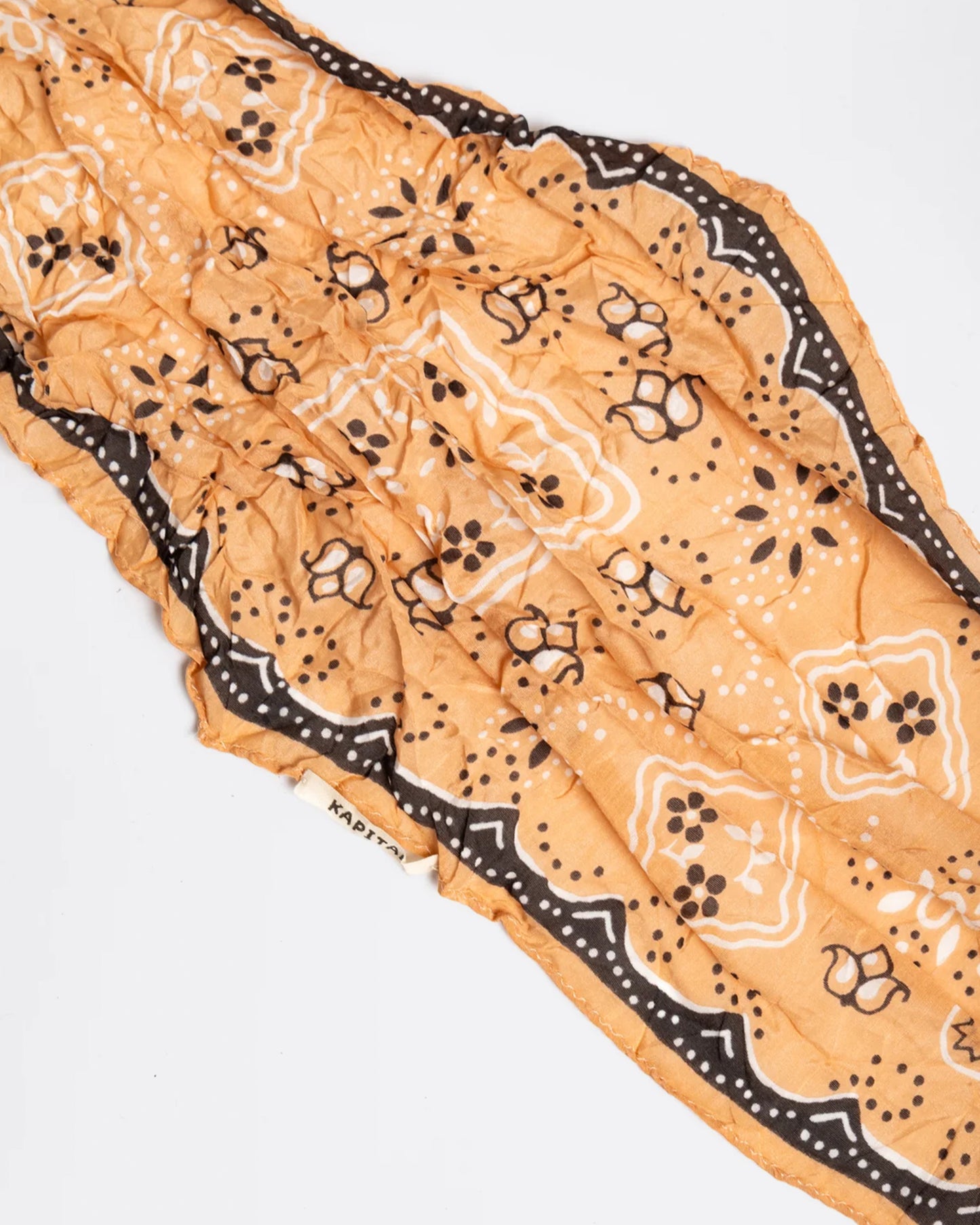 A peach colored diamond-shaped neckerchief with a paisley motif. Shown close up lying flat.