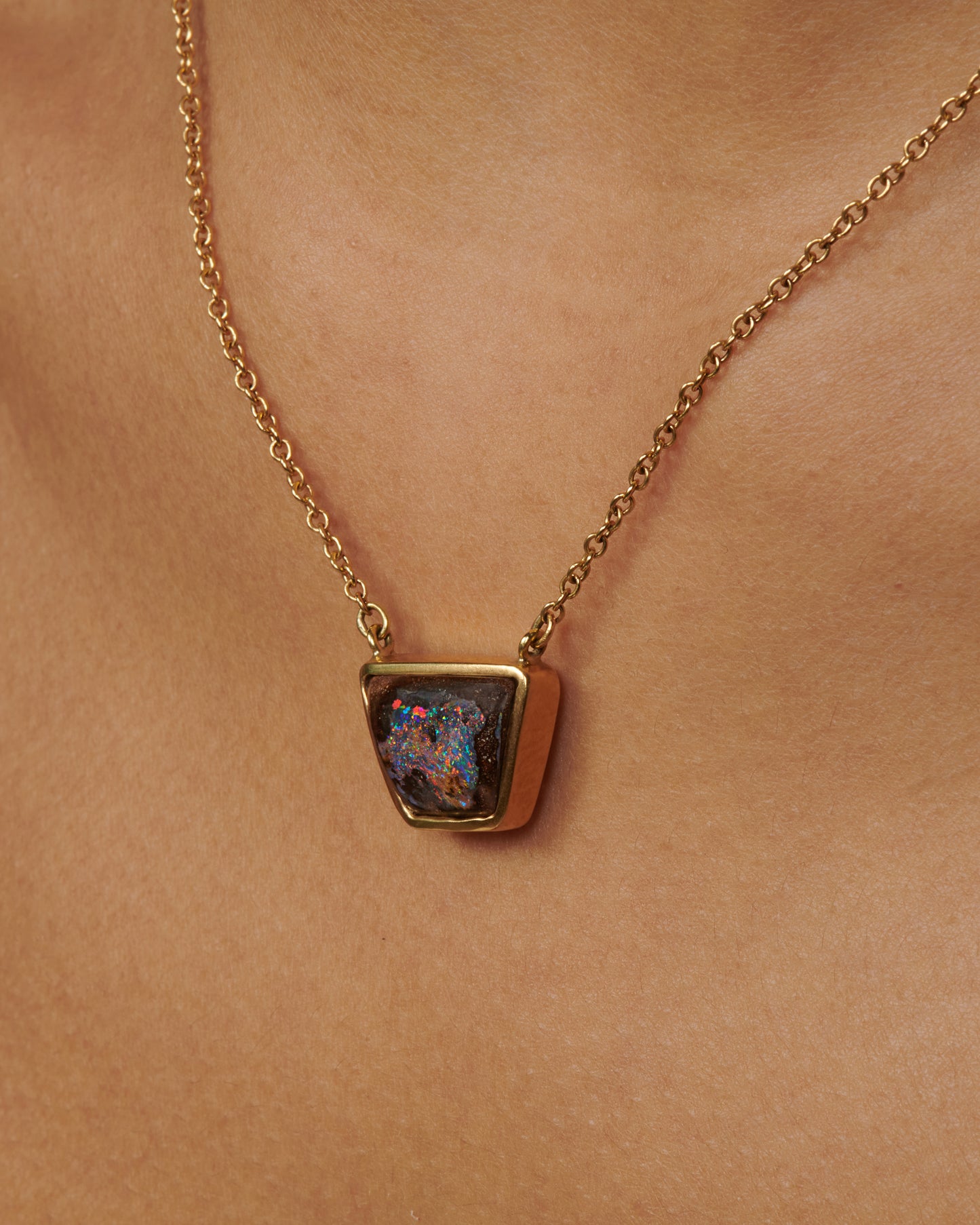 A yellow gold cable chain necklace with a trapezoidal opal set in a bezel. Shown from the side on a person.
