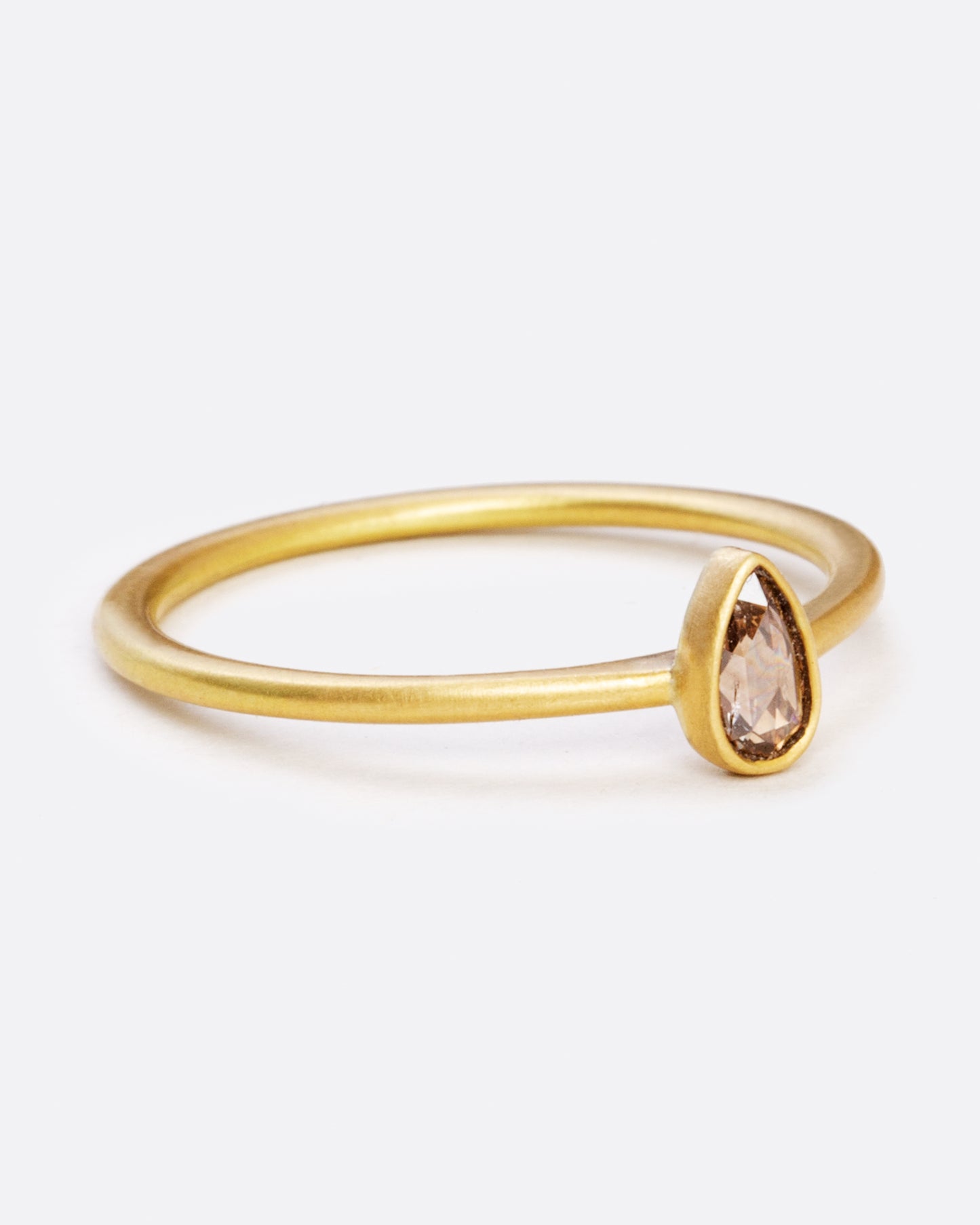 A yellow gold ring with a bezel set teardrop shaped diamond. Shown from the side.