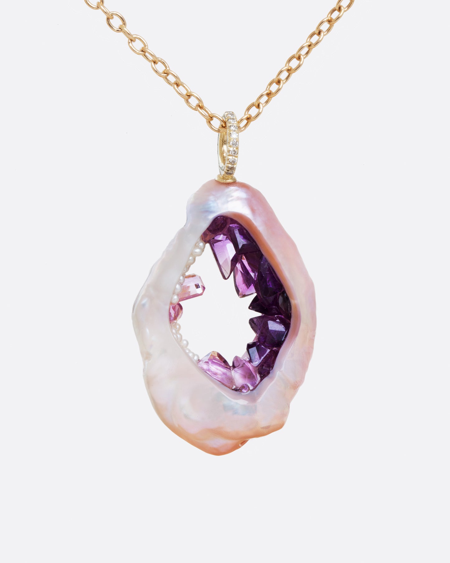 A large soufflé pearl open in the center and filled with pearls and amethysts, hanging from a cable chain and diamond bail. Shown from the front.