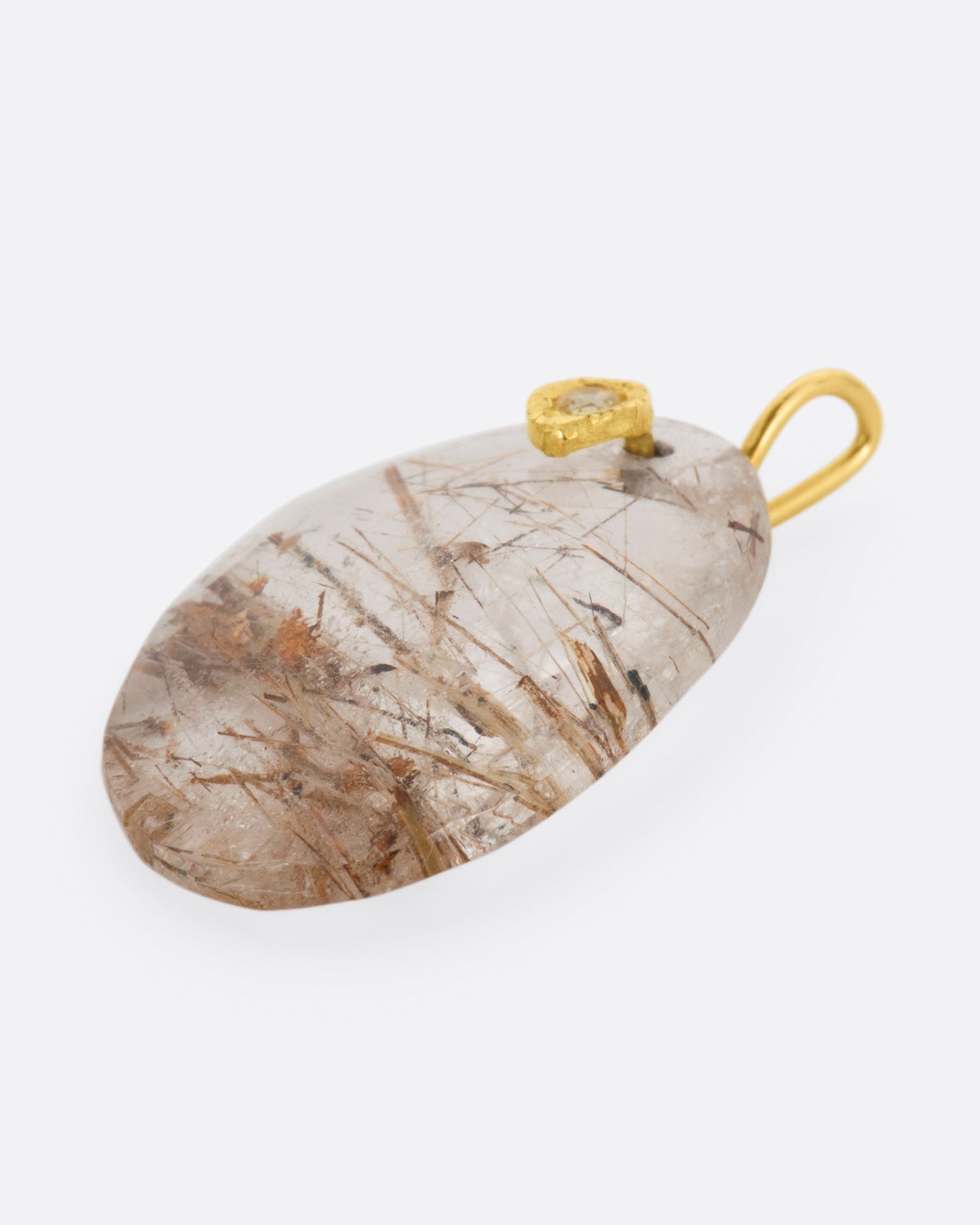 A yellow gold charm featuring a slice of rutilated quartz, with a yellow sapphire at its center. Shown from the side.