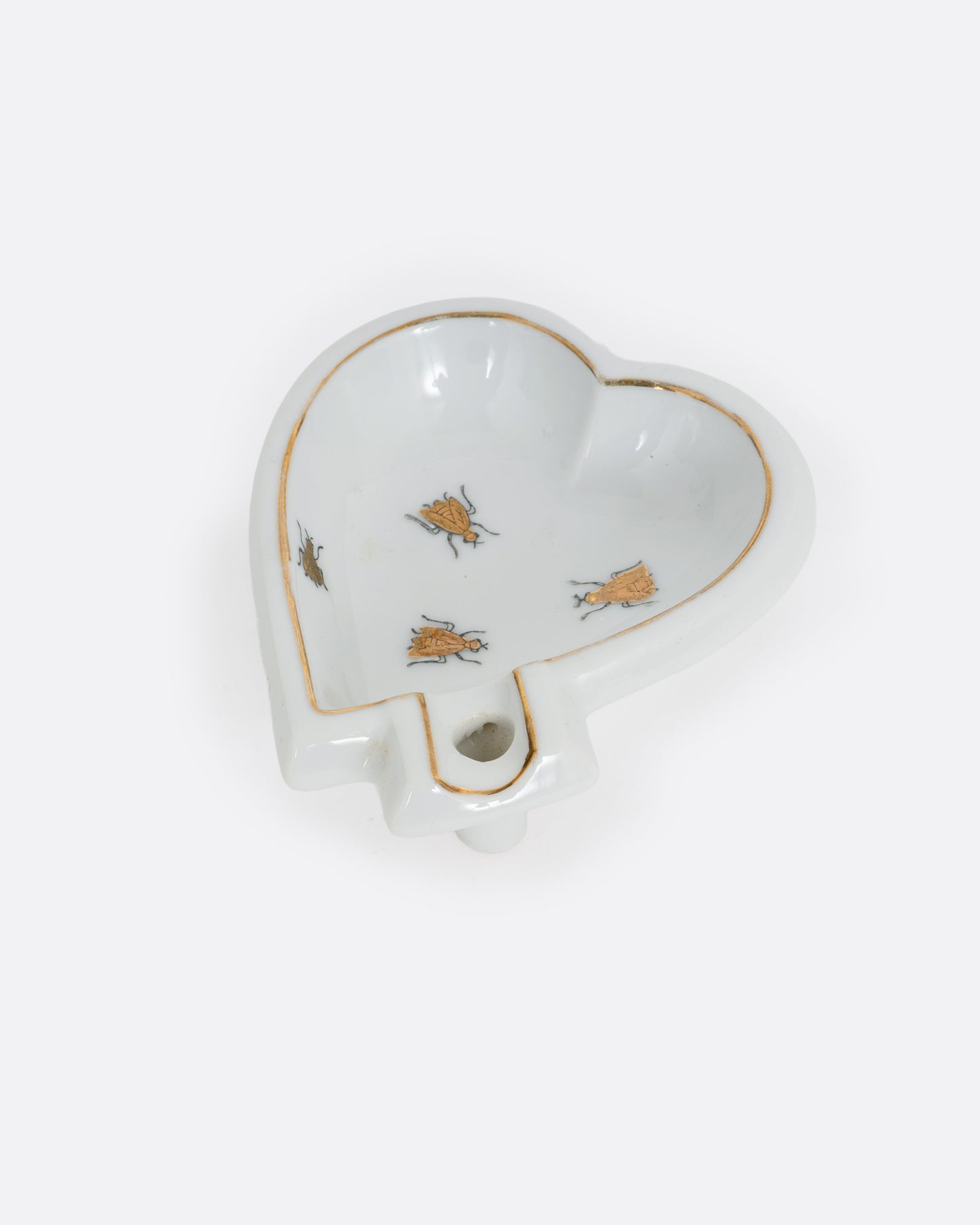 A heart shaped white ceramic dish with gold trim and bug designs. Shown at an angle from the top.
