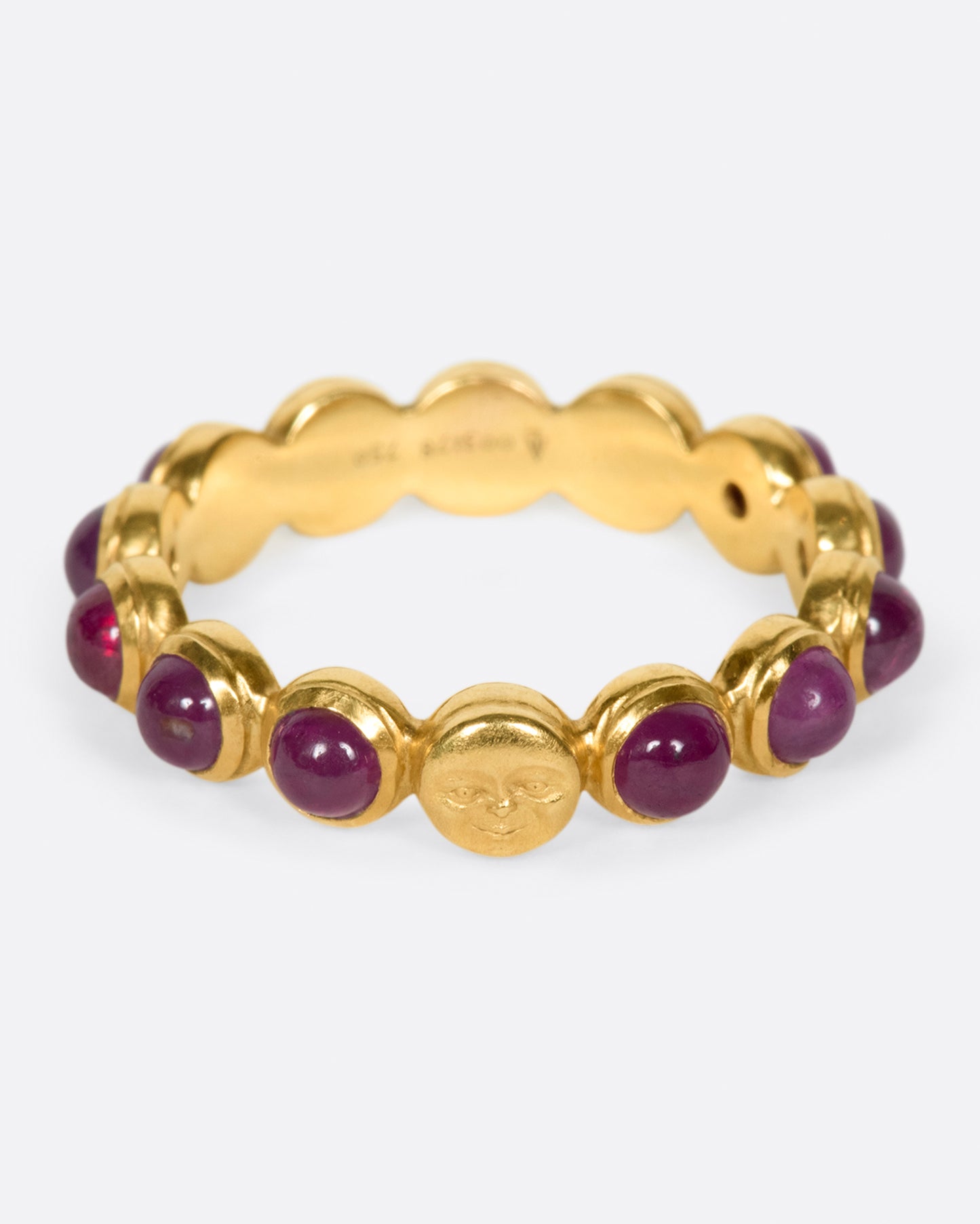 A yellow gold eternity band with ruby cabochons and one moonface. Shown from the front.