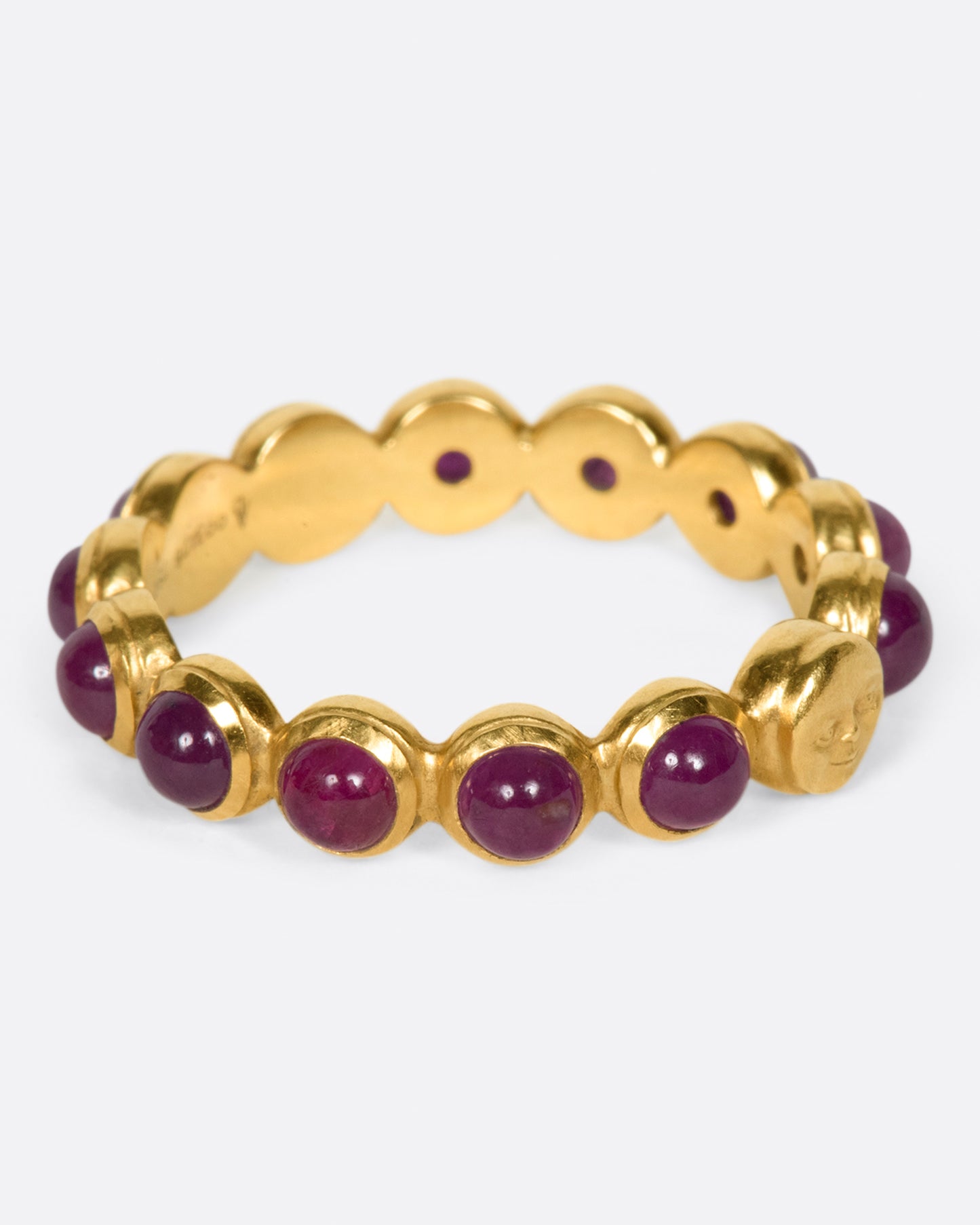 A yellow gold eternity band with ruby cabochons and one moonface. Shown from the side.