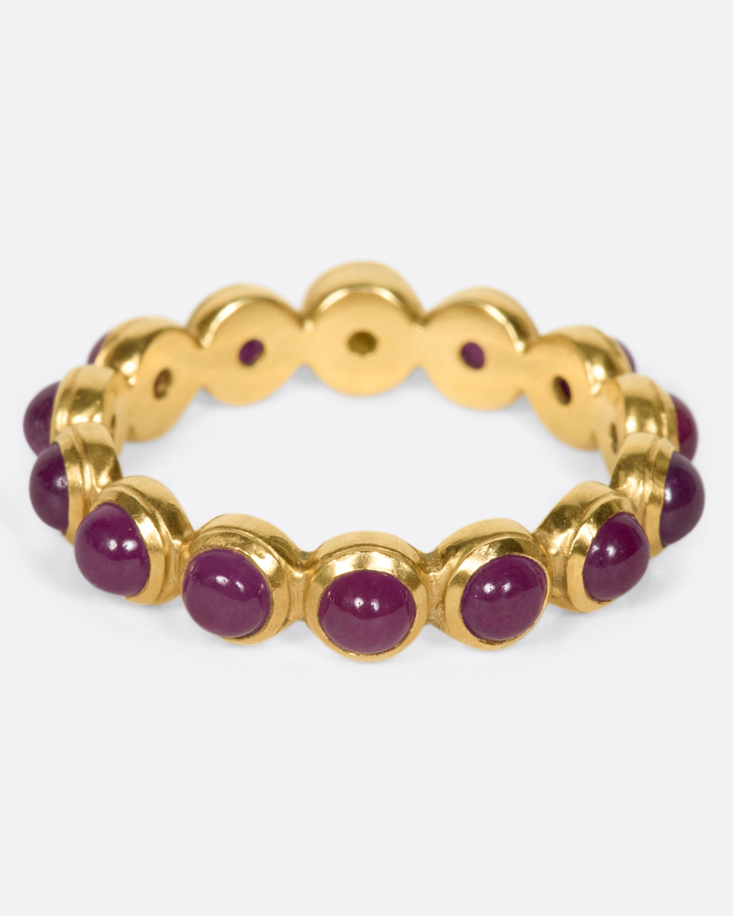 A yellow gold eternity band with ruby cabochons and one moonface. Shown from the back.