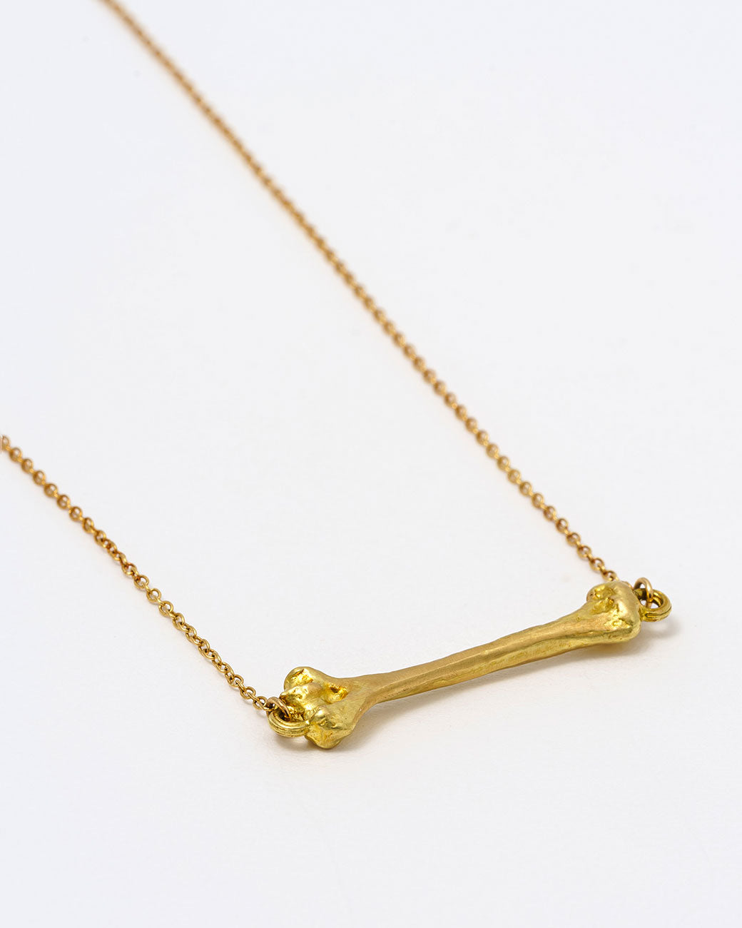A yellow gold cable chain necklace with a bone charm horizontally suspended from the center. Shown lying flat at an angle from the side.
