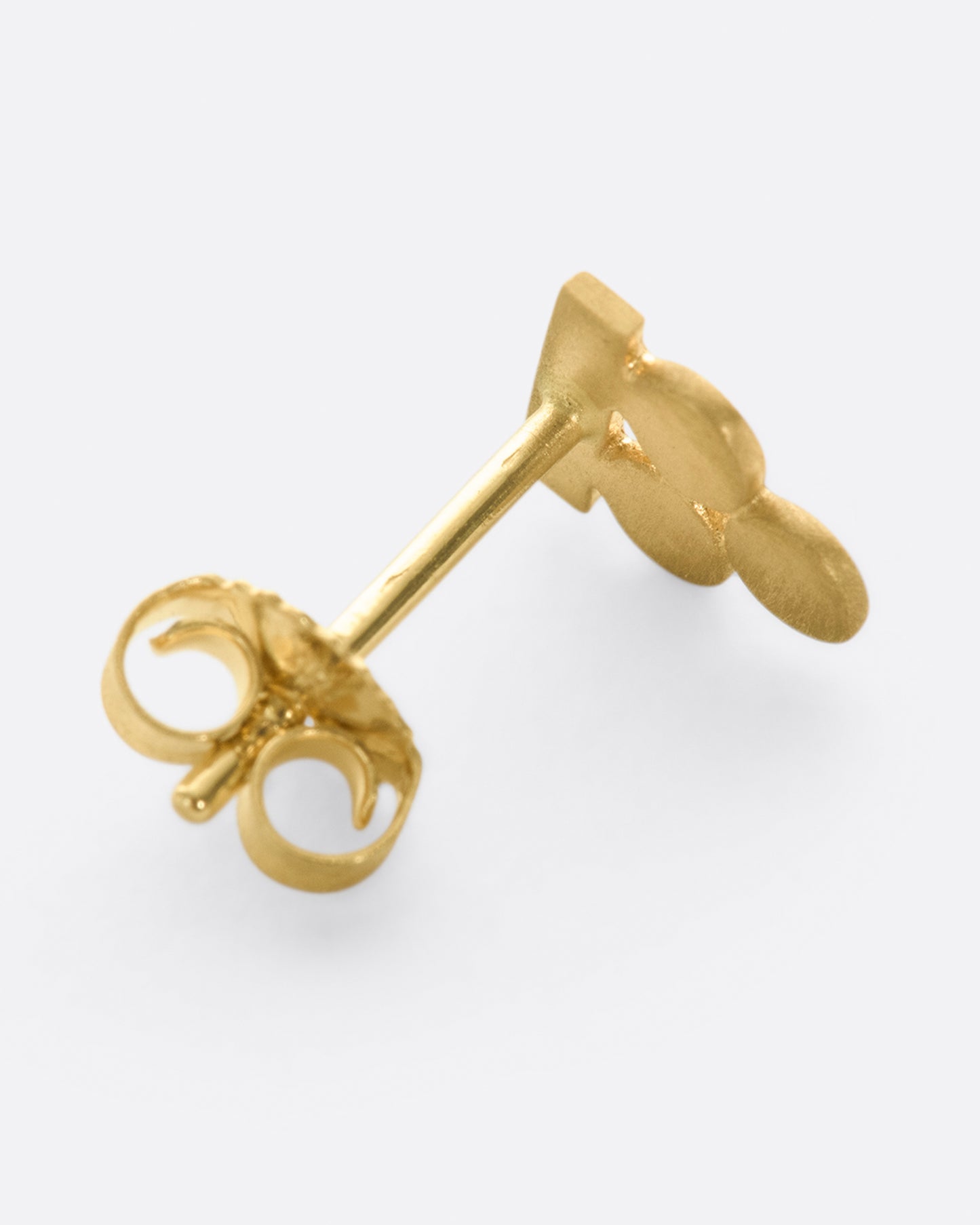 A yellow gold earring with three matte circles sitting on a bar. Shown lying flat from the back.