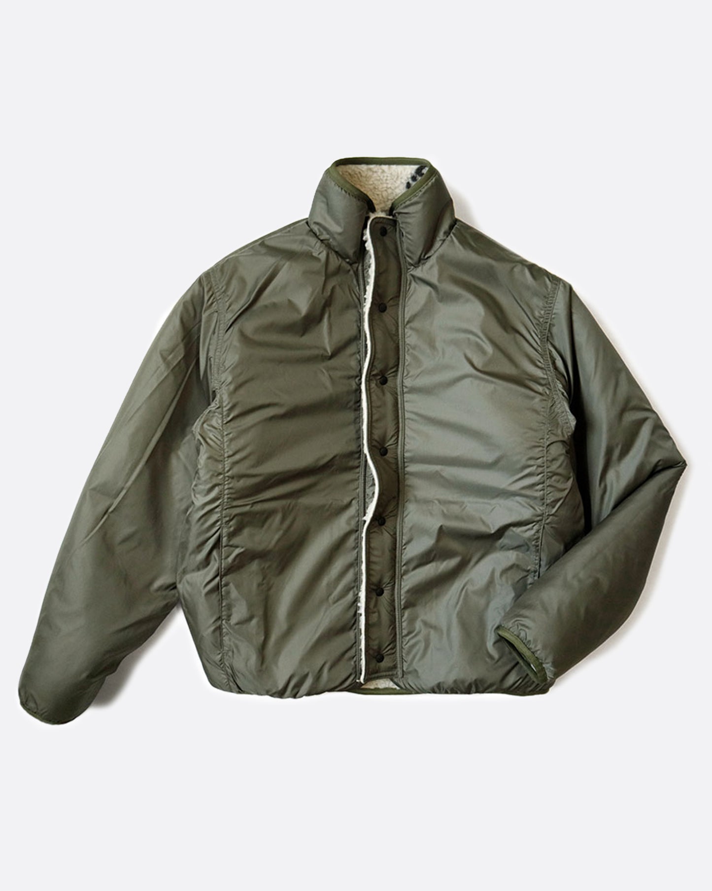 A reverisble jacket with white Beni Ourain patterned fleece on one side and a green nylon shell on the other, shown laying flat on the nylon side.