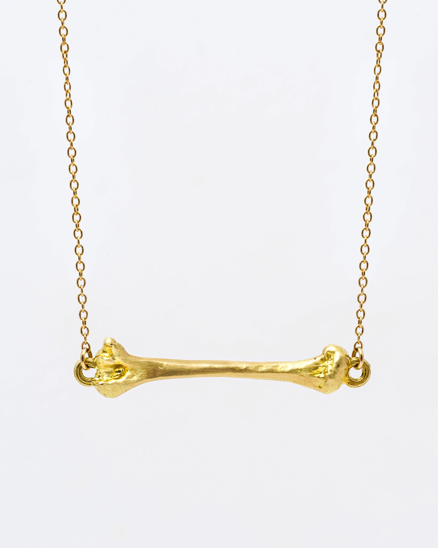 A yellow gold cable chain necklace with a bone charm horizontally suspended from the center. Shown from the front.