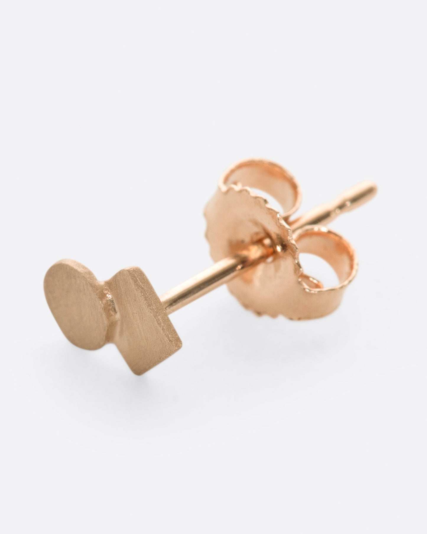 A rose gold square stud earring with overlapping circle and matte finish. Shown diagonally from the side.