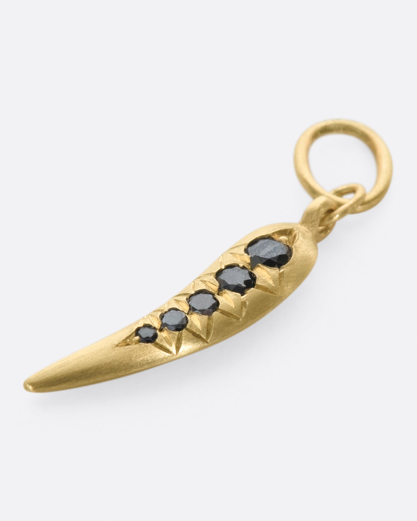 A yellow gold chili shaped charm with five graduated black diamonds. Shown laying flat.