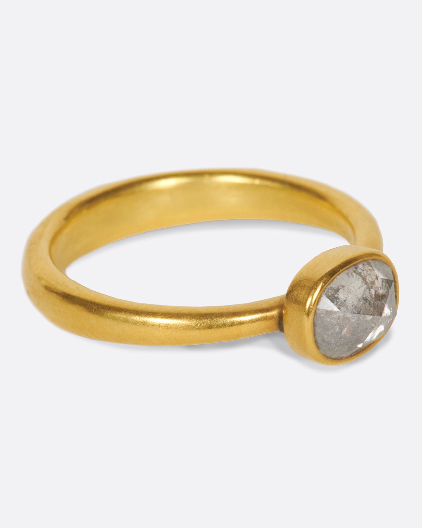 A pale grey, rose cut, oval diamond. Set horizontally on a simple, yellow gold band. Shown from the side.