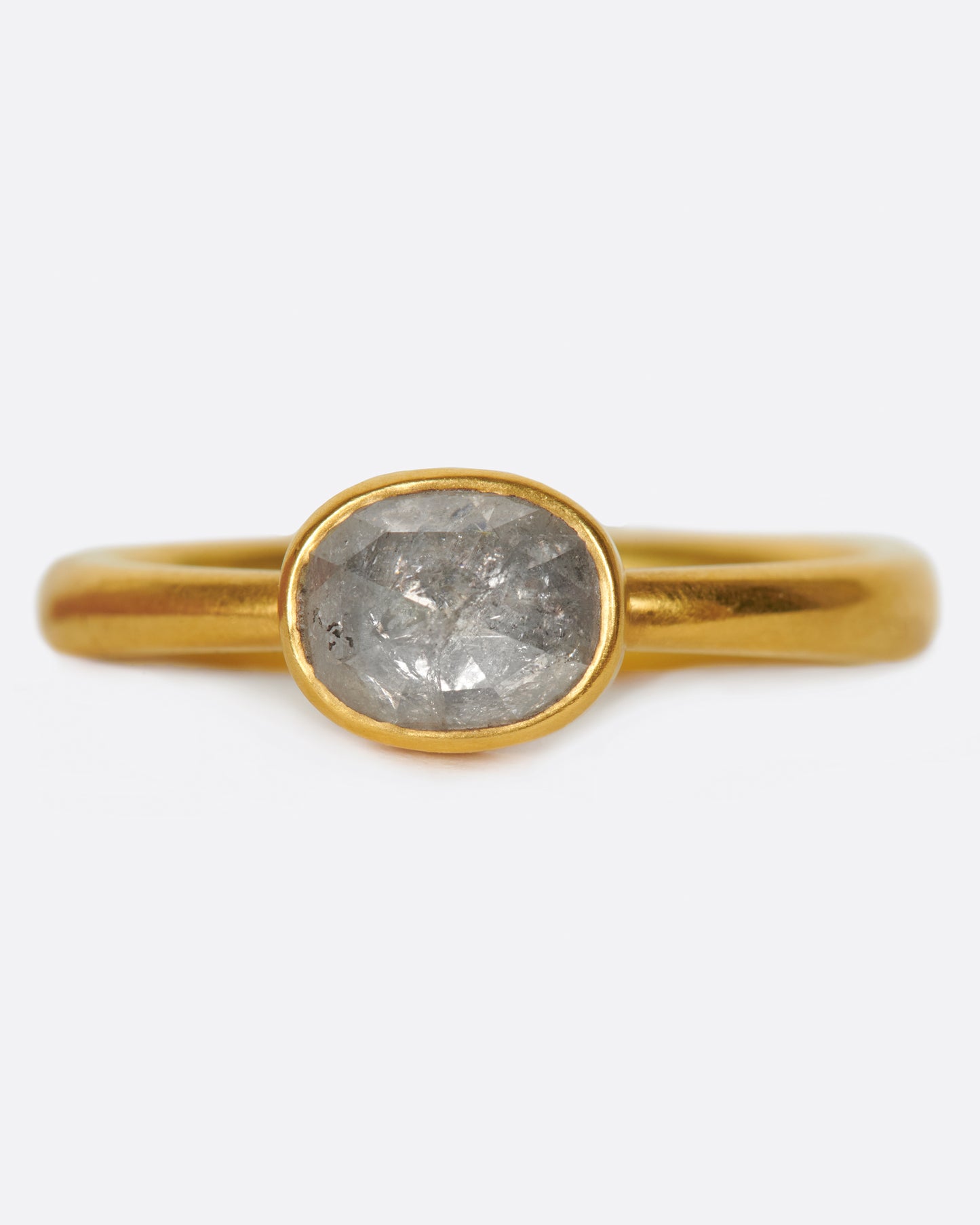 A pale grey, rose cut, oval diamond. Set horizontally on a simple, yellow gold band. Shown from the front.