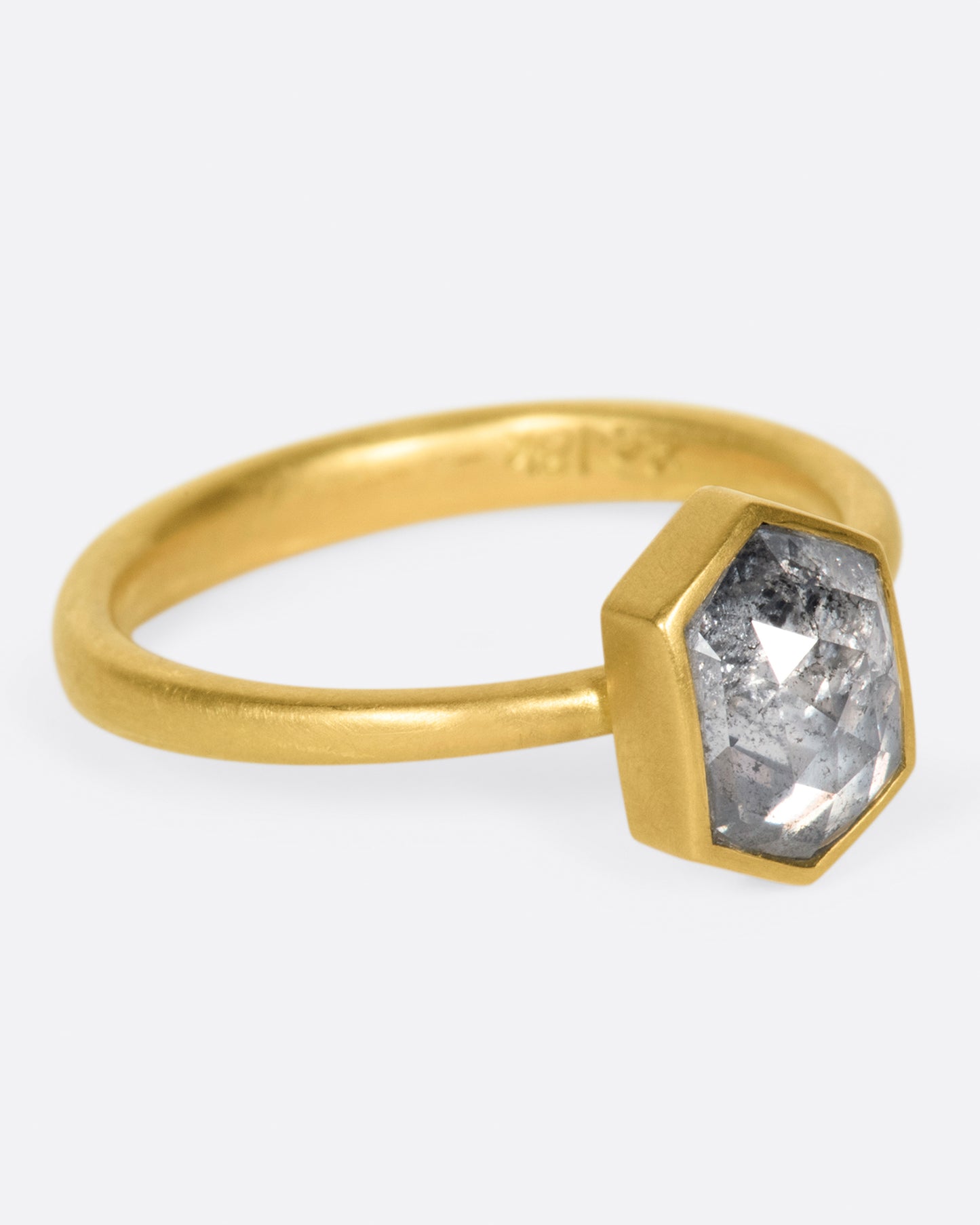 A yellow gold ring with a salt and pepper hexagonal diamond. Shown from the side.