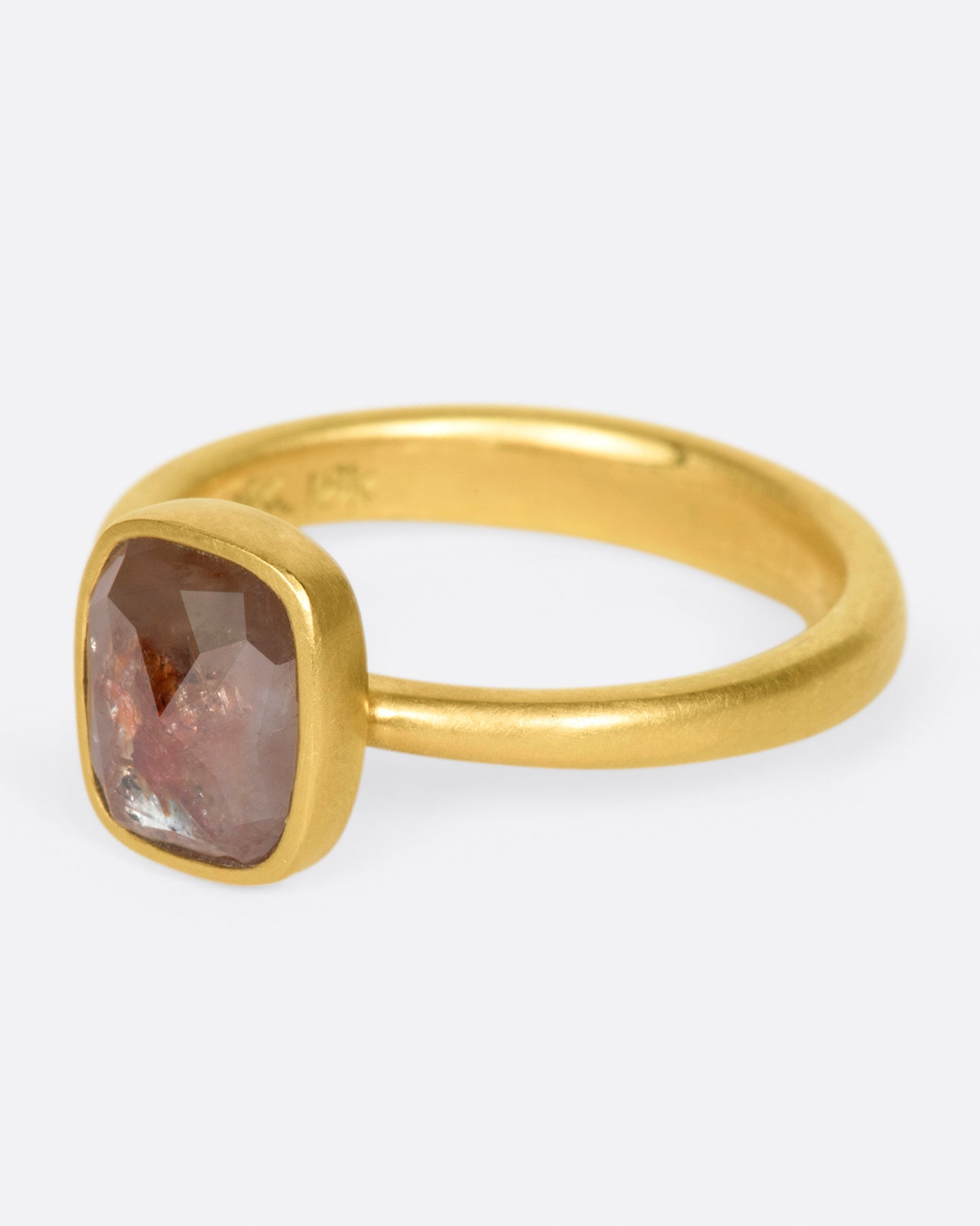 A yellow gold ring with a cushion shaped, rusty-red diamond. Shown from the side.