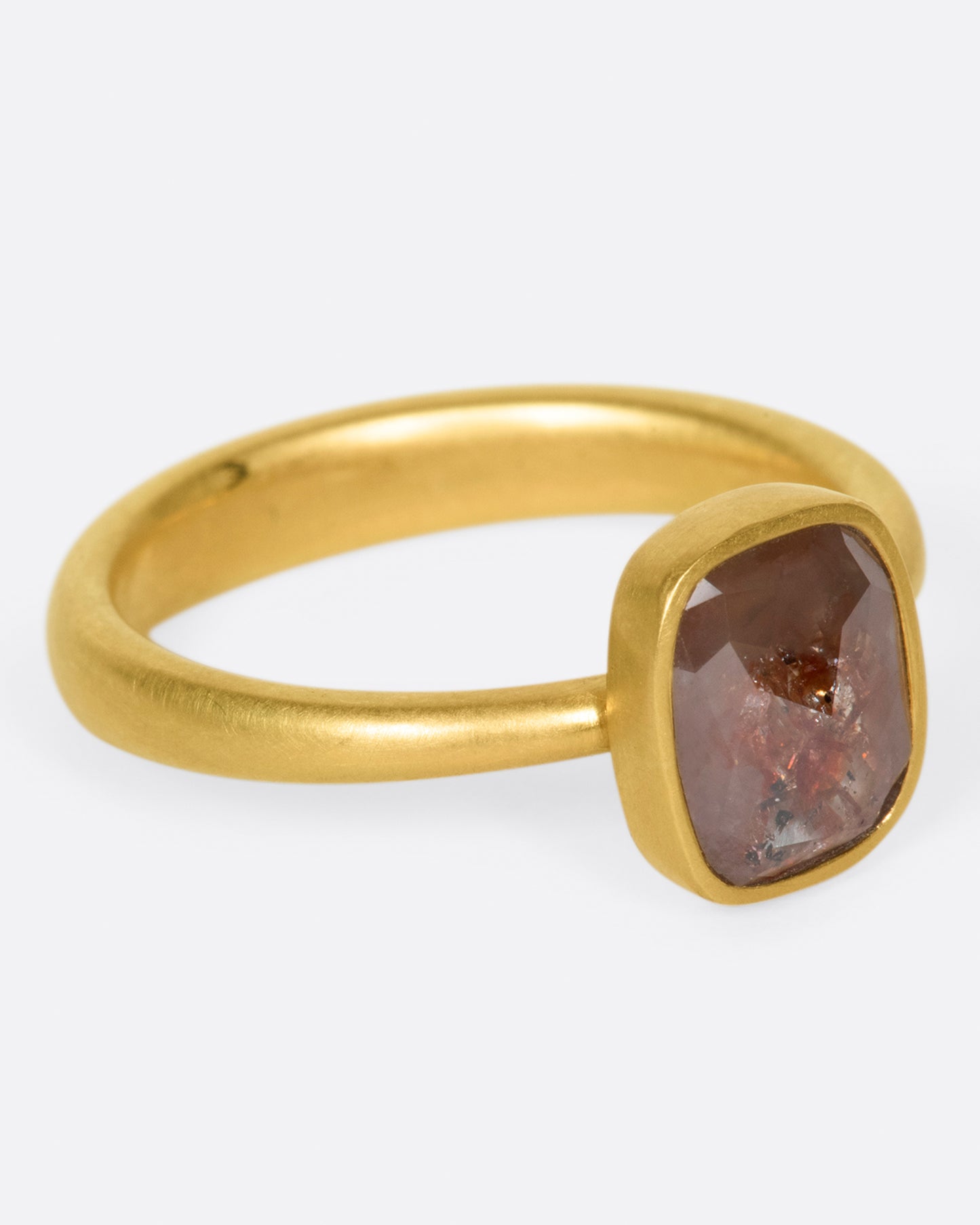 A yellow gold ring with a cushion shaped, rusty-red diamond. Shown from the side.