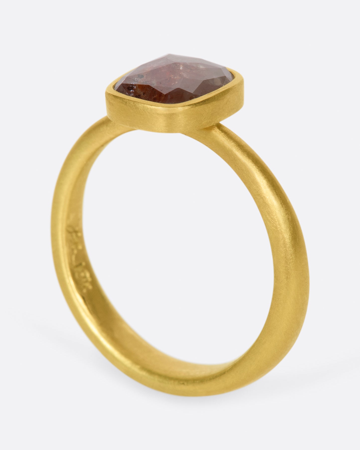 A yellow gold ring with a cushion shaped, rusty-red diamond. Shown standing up from the side.