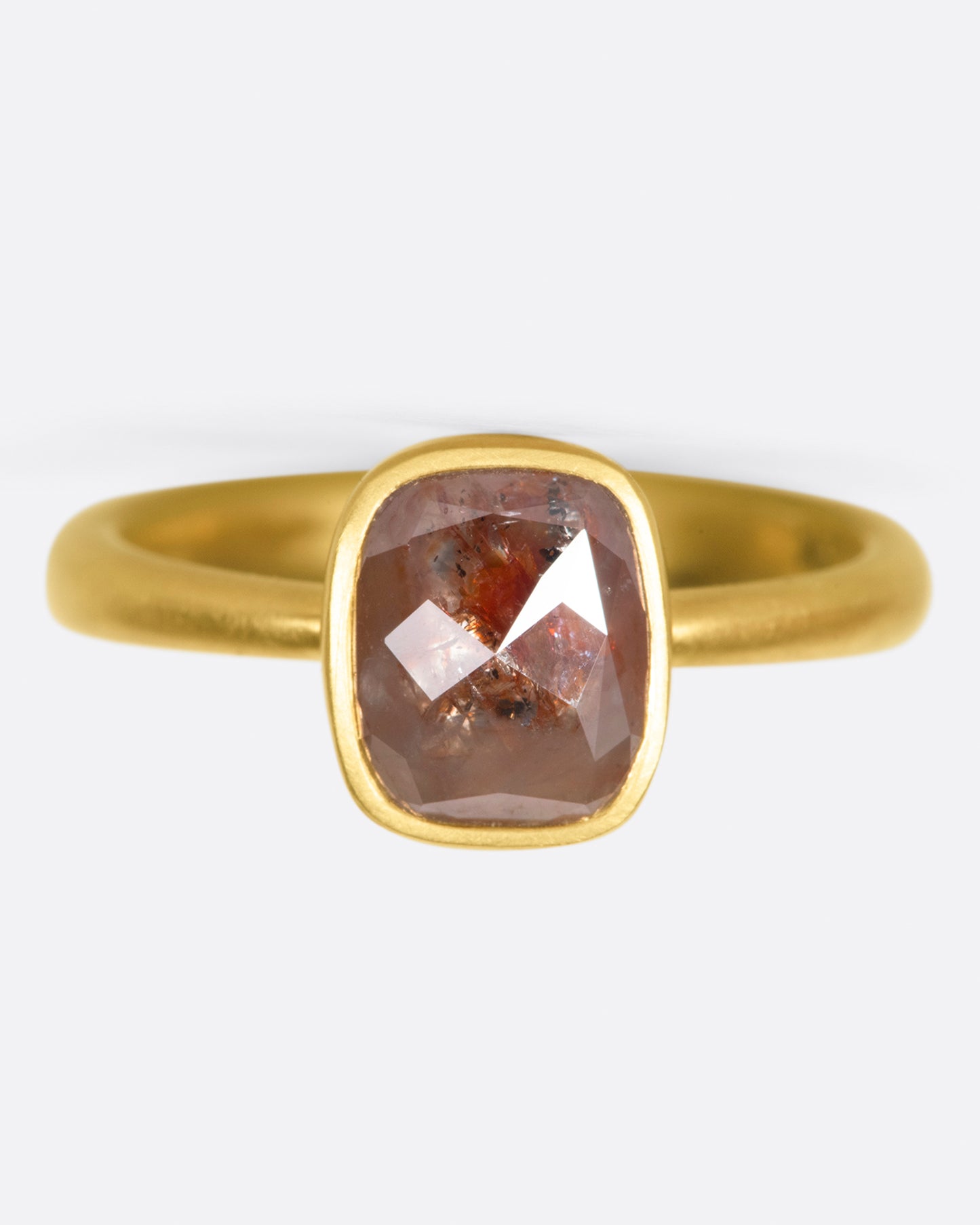 A yellow gold ring with a cushion shaped, rusty-red diamond. Shown from the front.