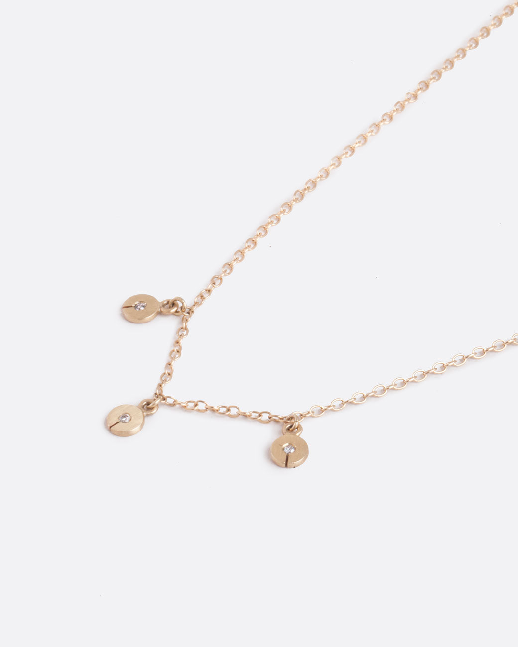 A yellow gold cable chain necklace with three disc charms. Each disc has a single gray diamond with a slit in the bottom. Shown diagonally from the front.