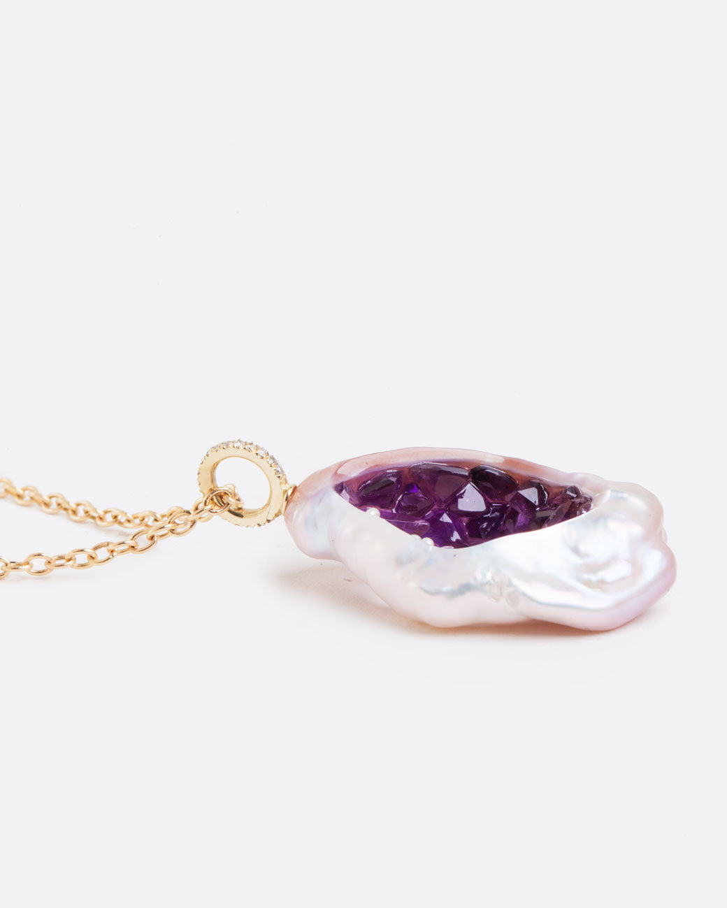 A large soufflé pearl open in the center and filled with pearls and amethysts, hanging from a cable chain and diamond bail. Shown from the side lying flat.