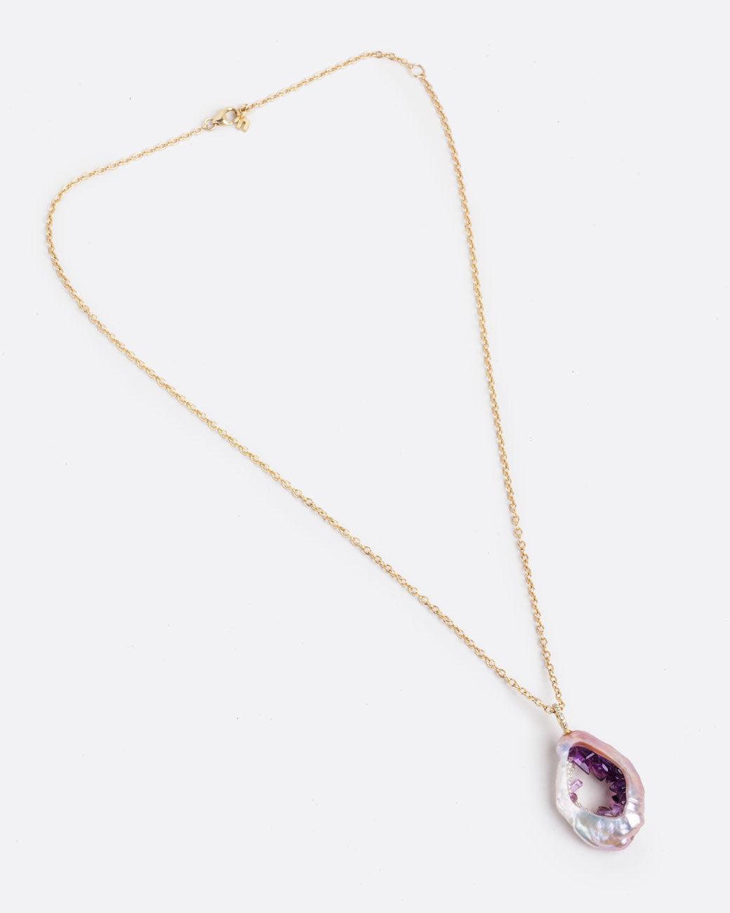 A large soufflé pearl open in the center and filled with pearls and amethysts, hanging from a cable chain and diamond bail. Shown lying flat from the front with clasp closed.
