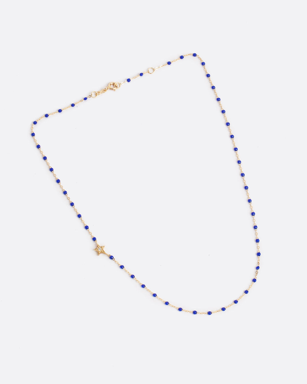 Layflat birds eye view of yellow gold chain necklace with dark blue resin beads and off centered yellow gold star with diamond center with clasp closed