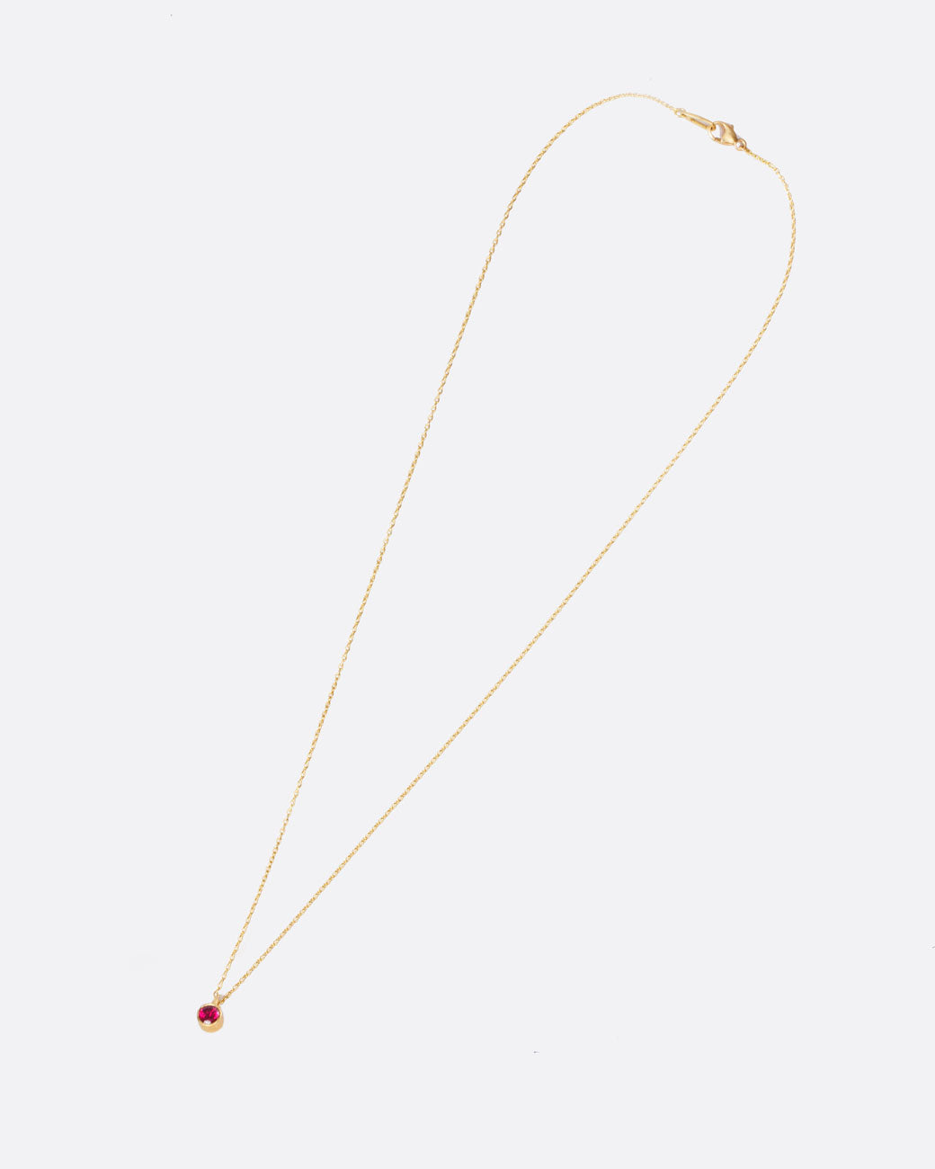 A yellow gold cable chain necklace with a round bezel set ruby pendant. Shown closed lying flat diagonally from the front.